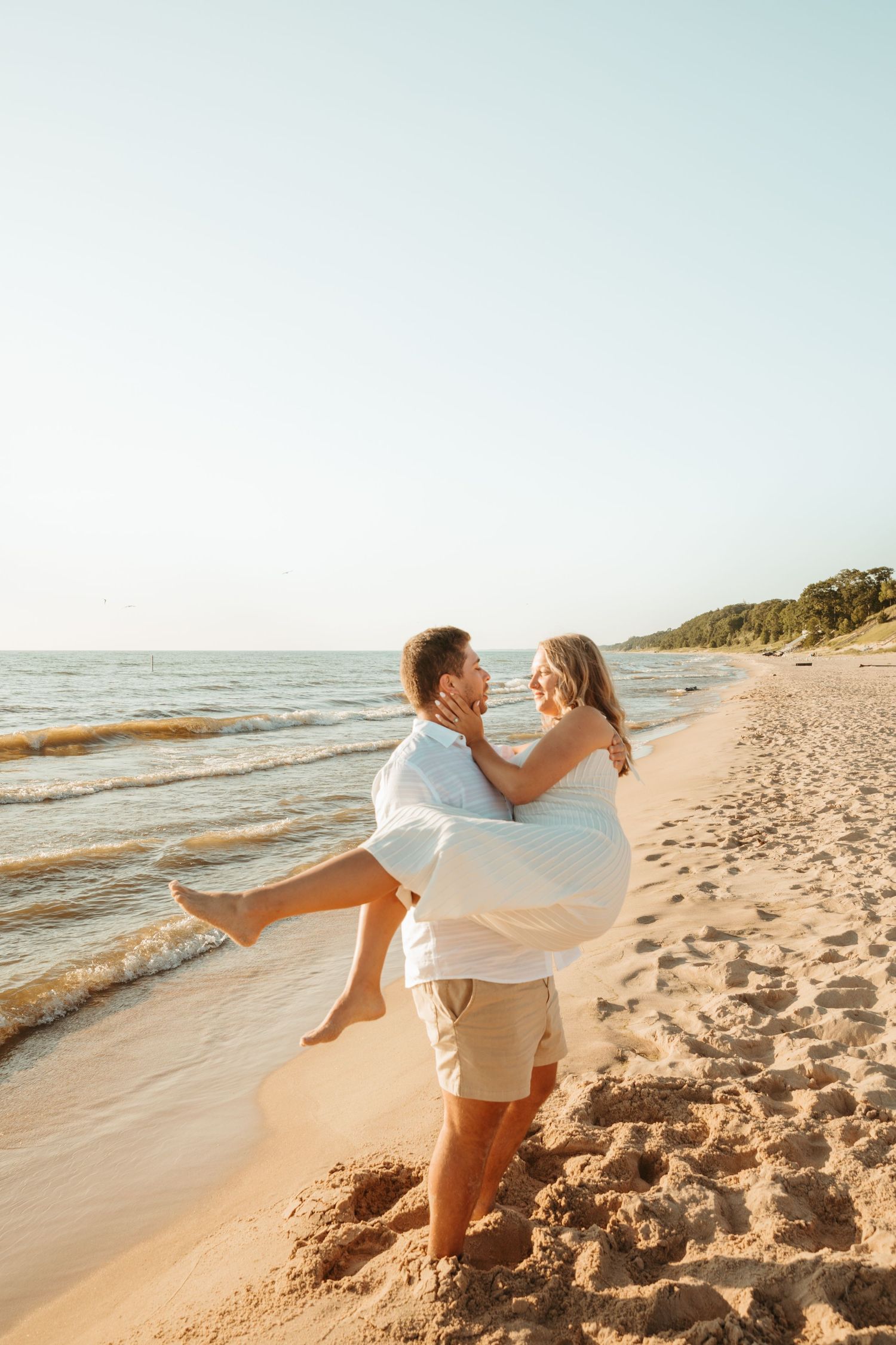 Couple performing romantic dance lift on sandy beach with ocean waves behind them.