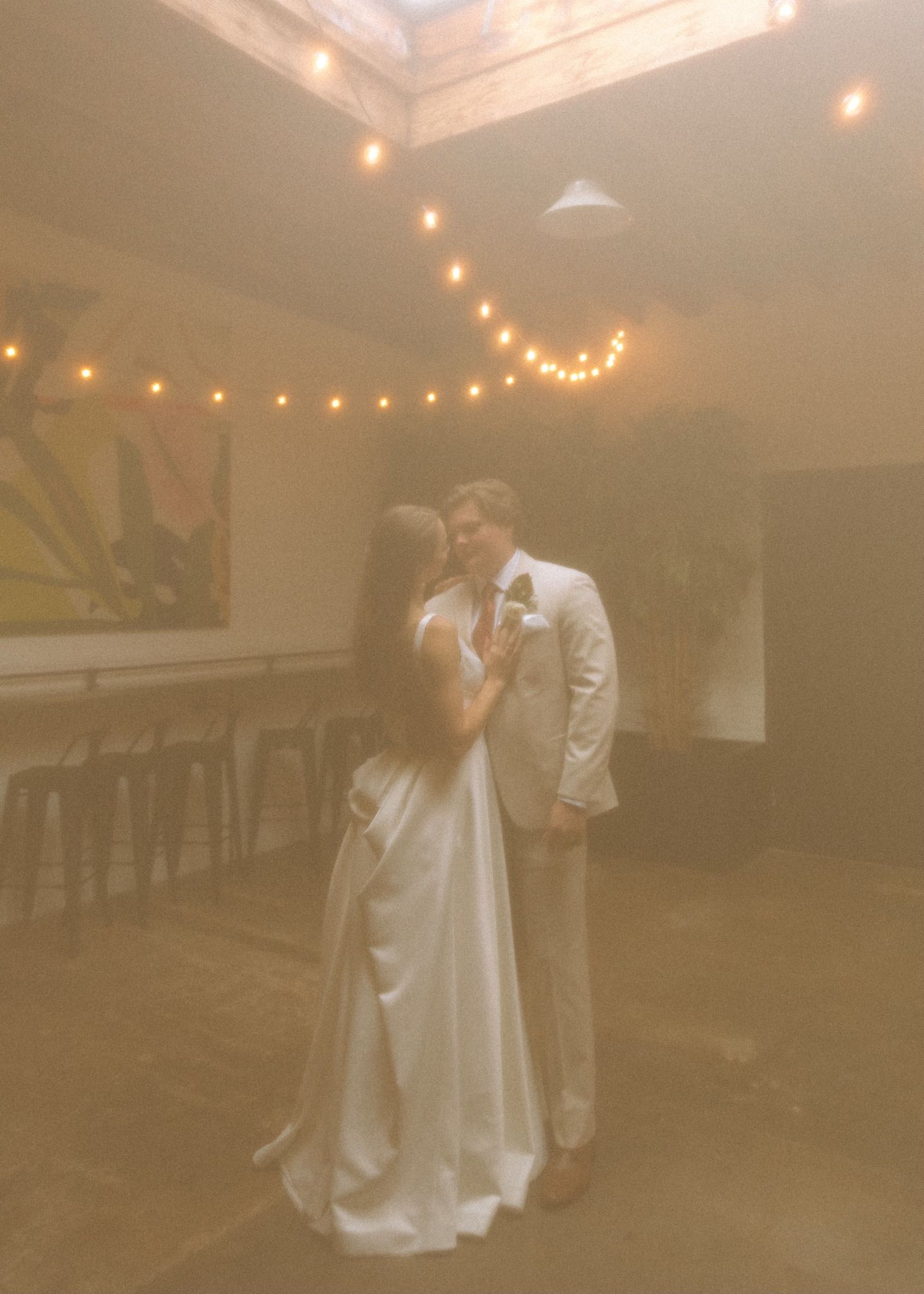 Wedding couple dancing in elegant venue decorated with string lights.