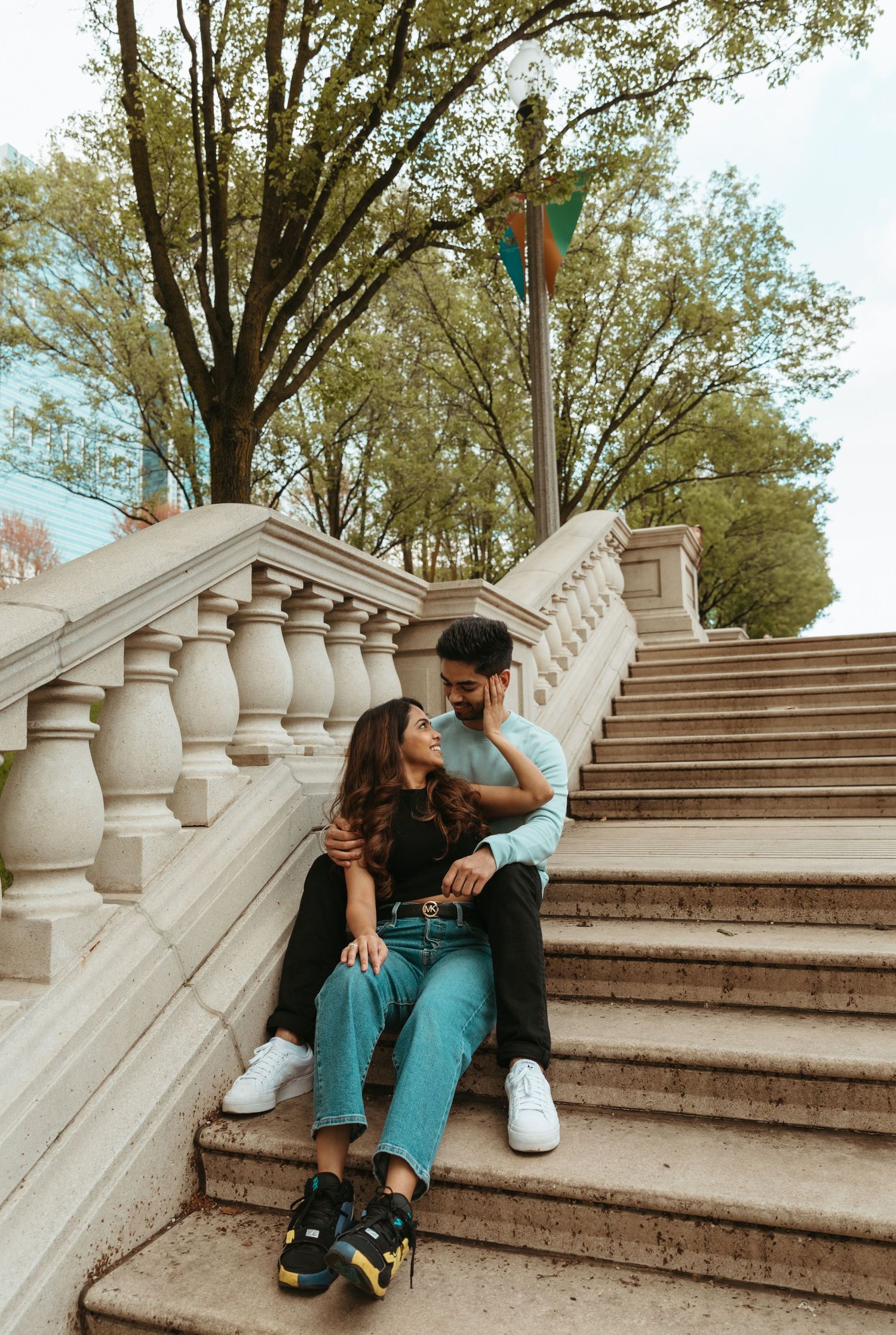 A couple sits together on white stone steps outdoors on an autumn day.