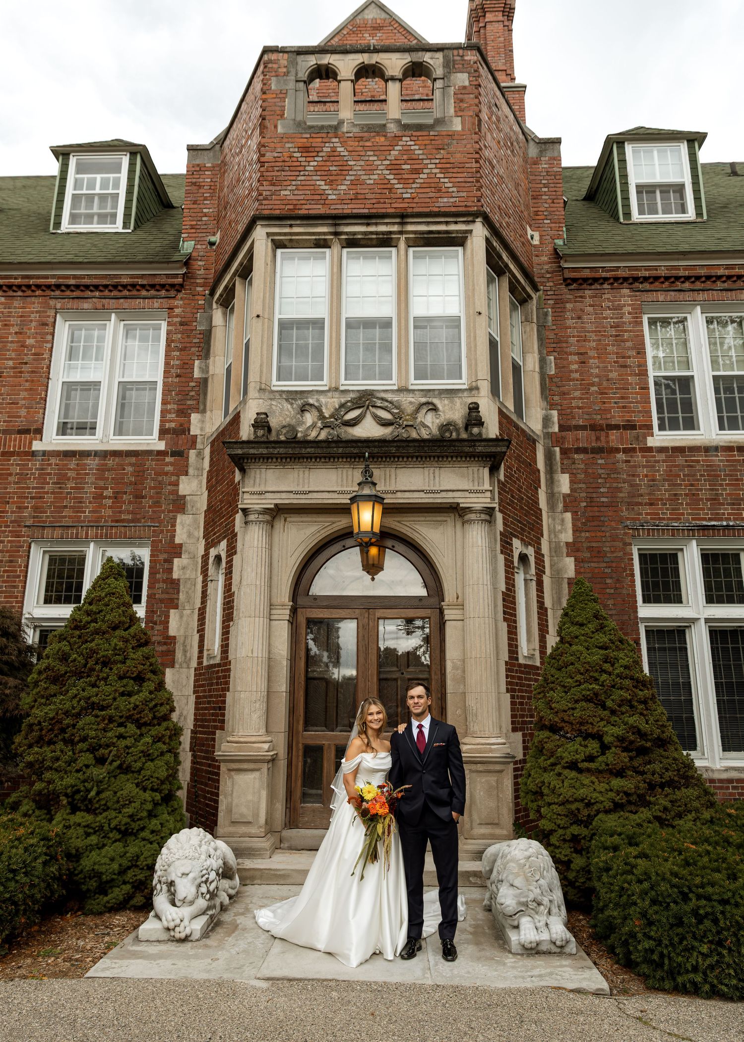Wedding couple poses in front of an elegant stone archway entrance with stone lion statues.