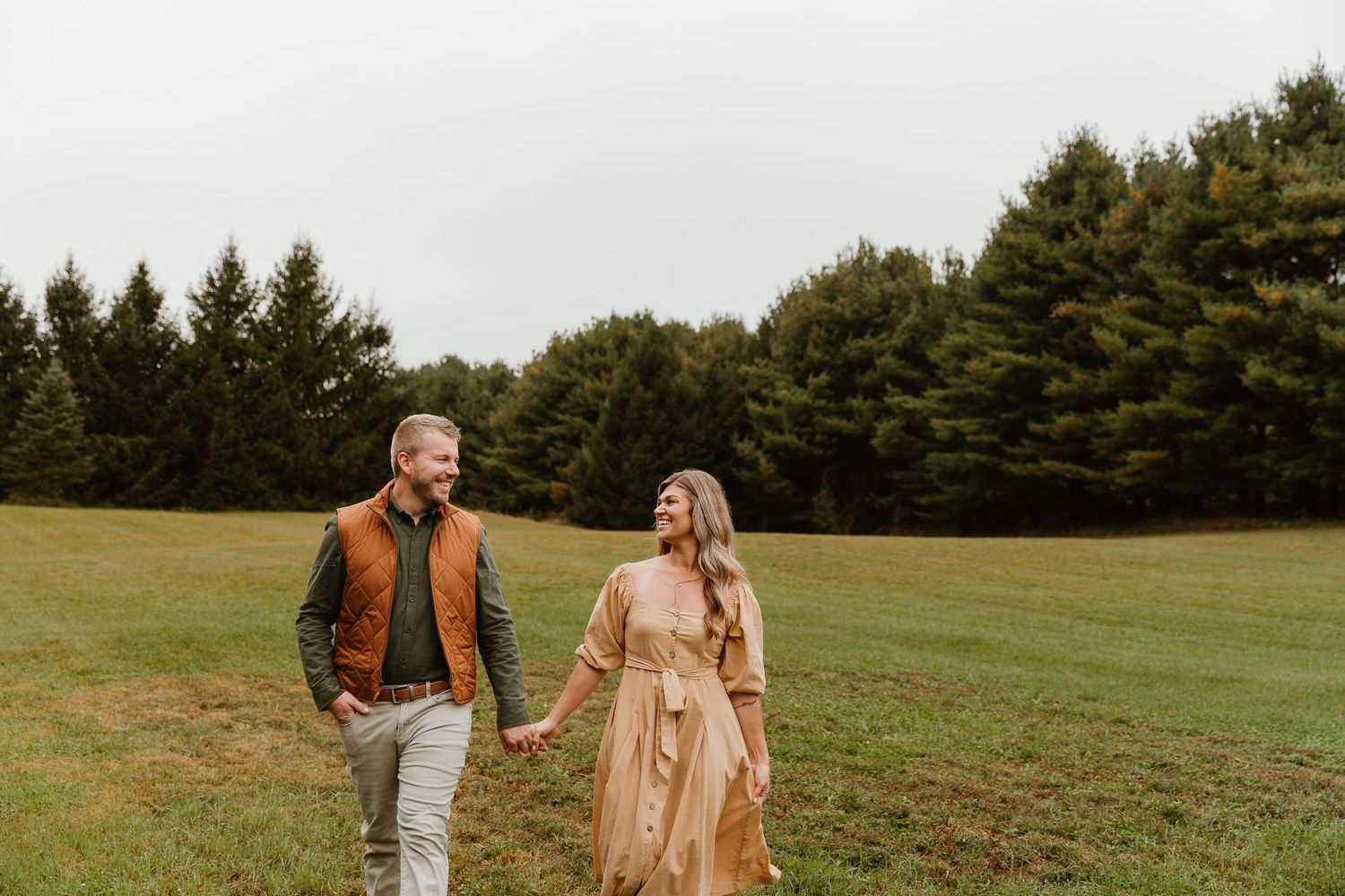 People and their dog enjoy a fall photoshoot in an open field with evergreen trees in background.
