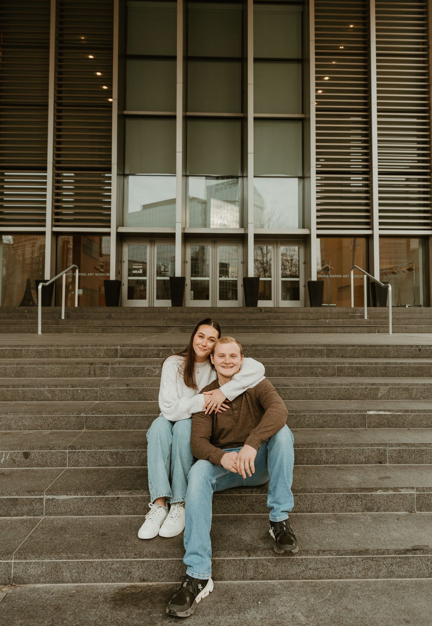 Two people relax on wide concrete steps in front of a contemporary building facade.