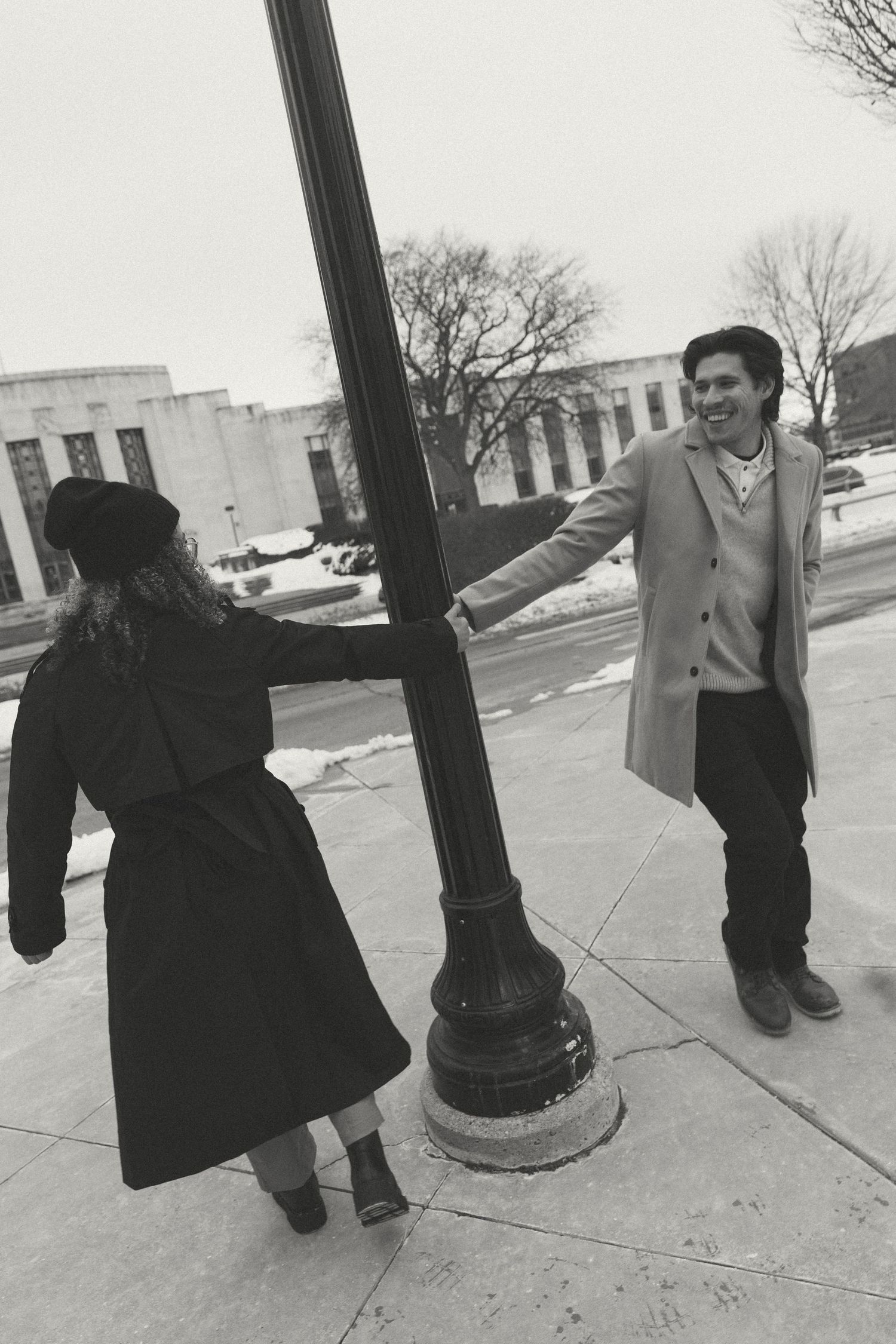 A black and white photo of a couple playing around a street lamp post.