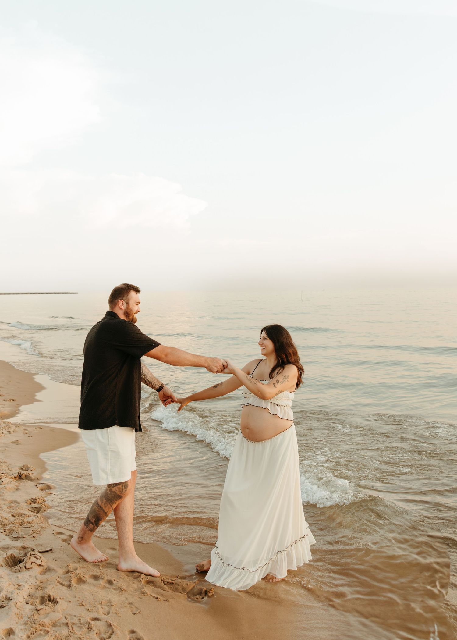 A couple dances together on a beach at sunset with waves gently rolling in the background.