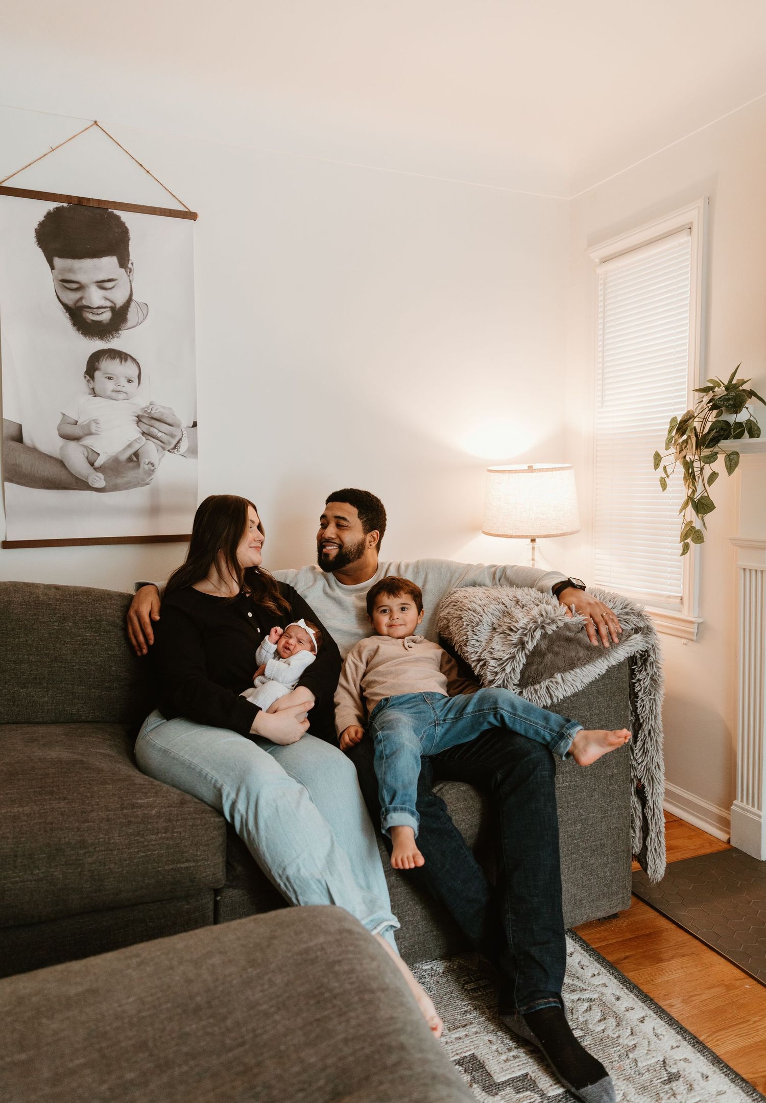 A family relaxes together on a grey couch in their living room with framed photos on the wall.