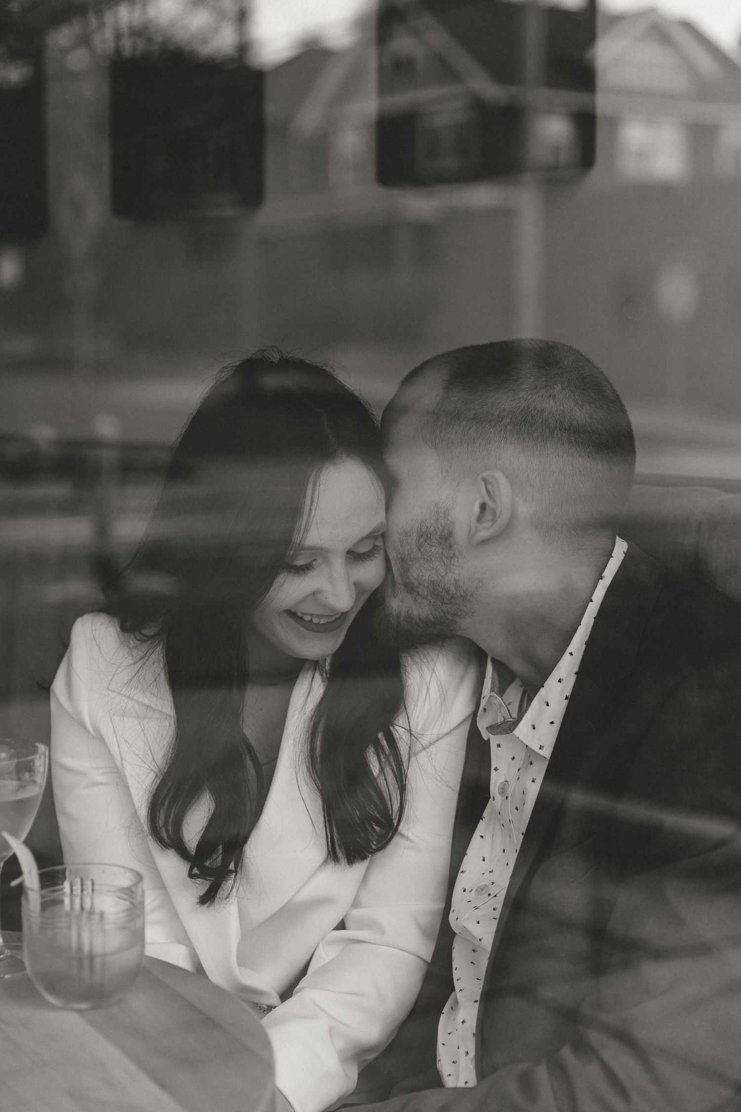 Romantic couple laughing together at cafe table through window glass.