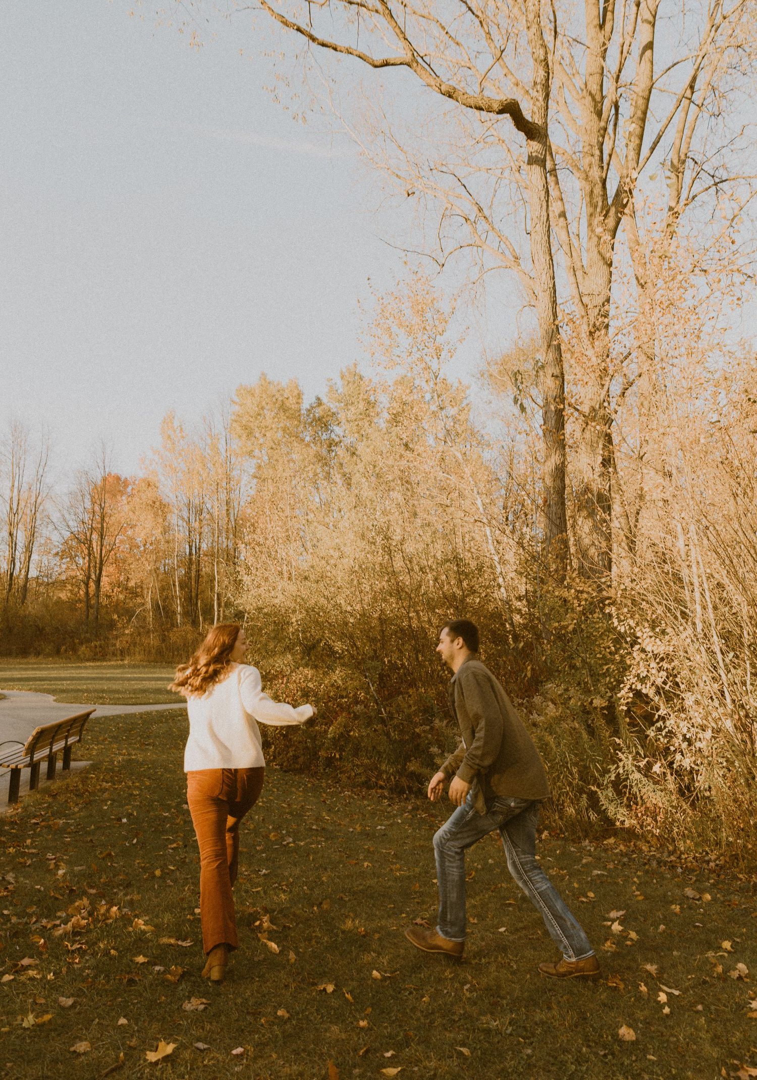 Playful couple running through fallen leaves on an autumn path.