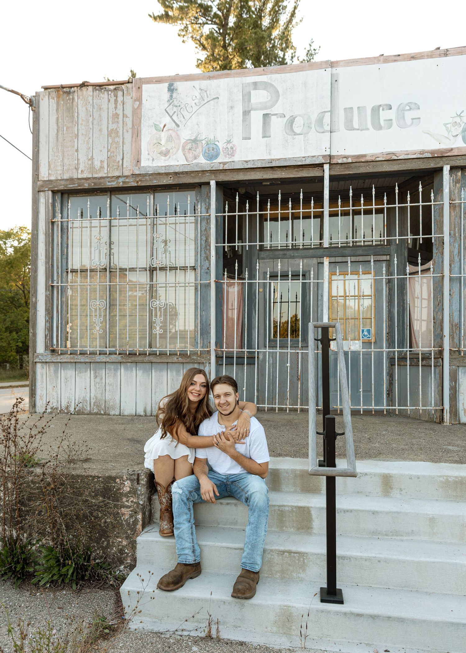 Casual couple poses together on steps of old produce store.