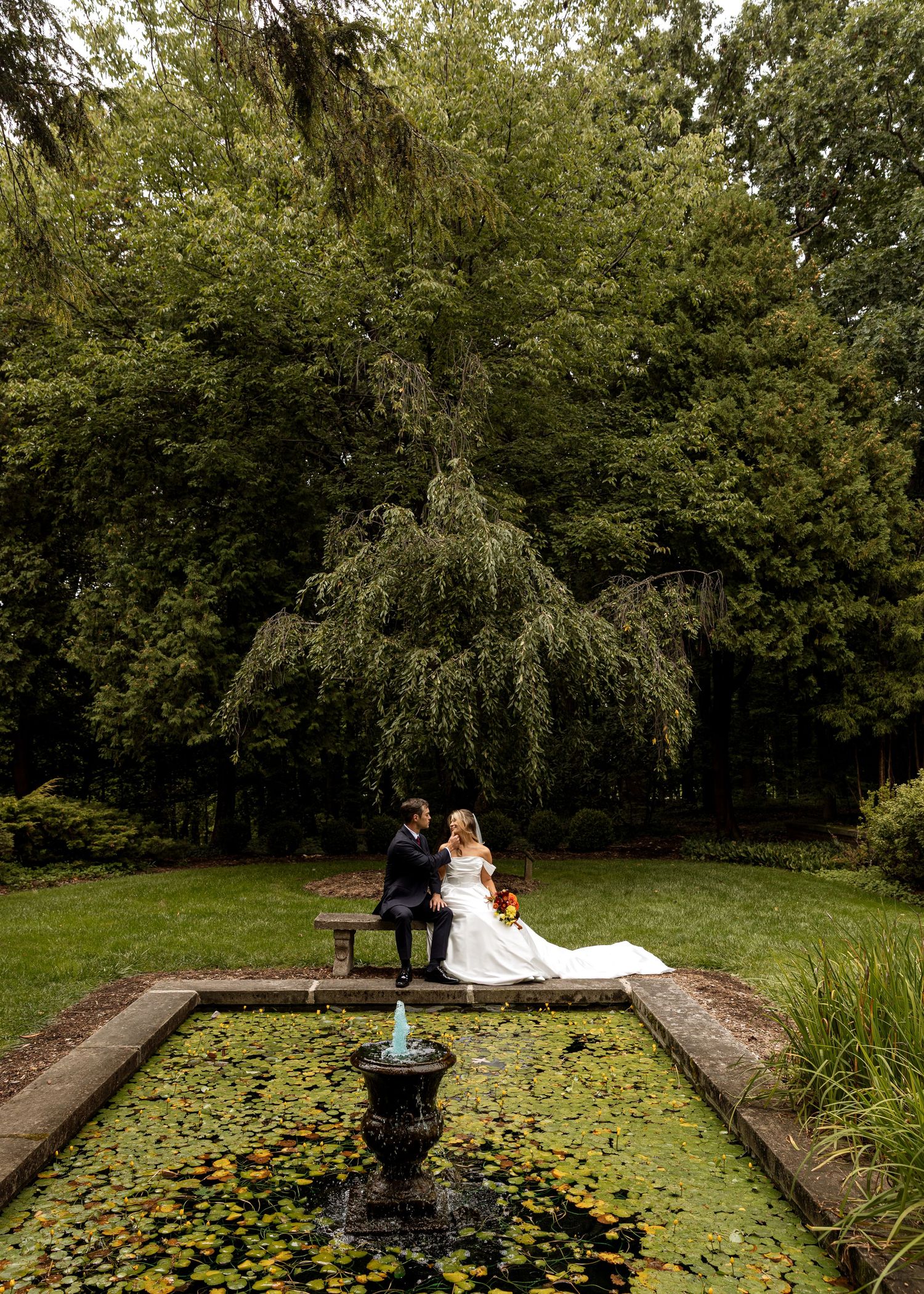 Progressive wedding photos near a garden pond with lily pads and fountain in a serene outdoor setting.