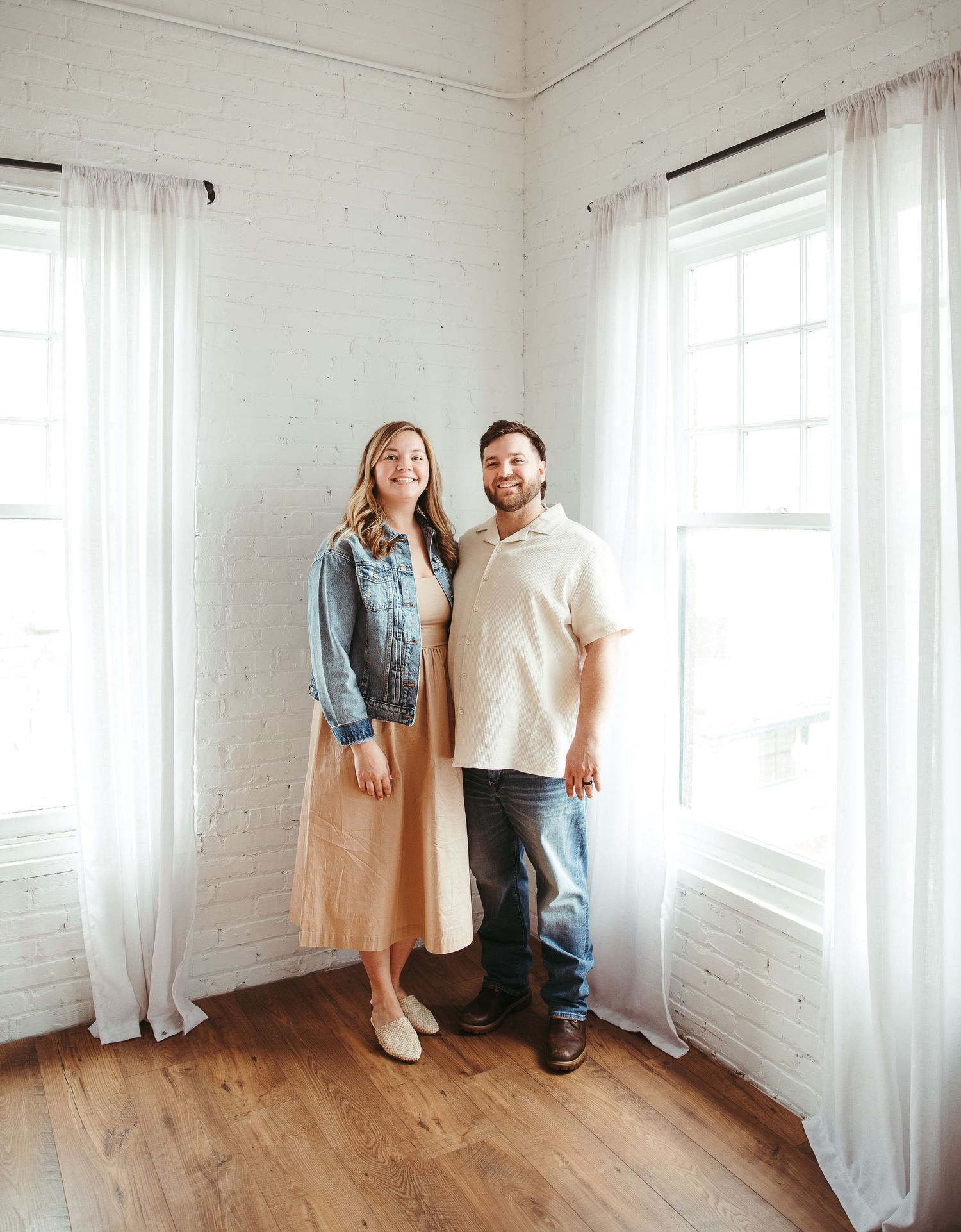 Family standing together in bright white room with hardwood floors.