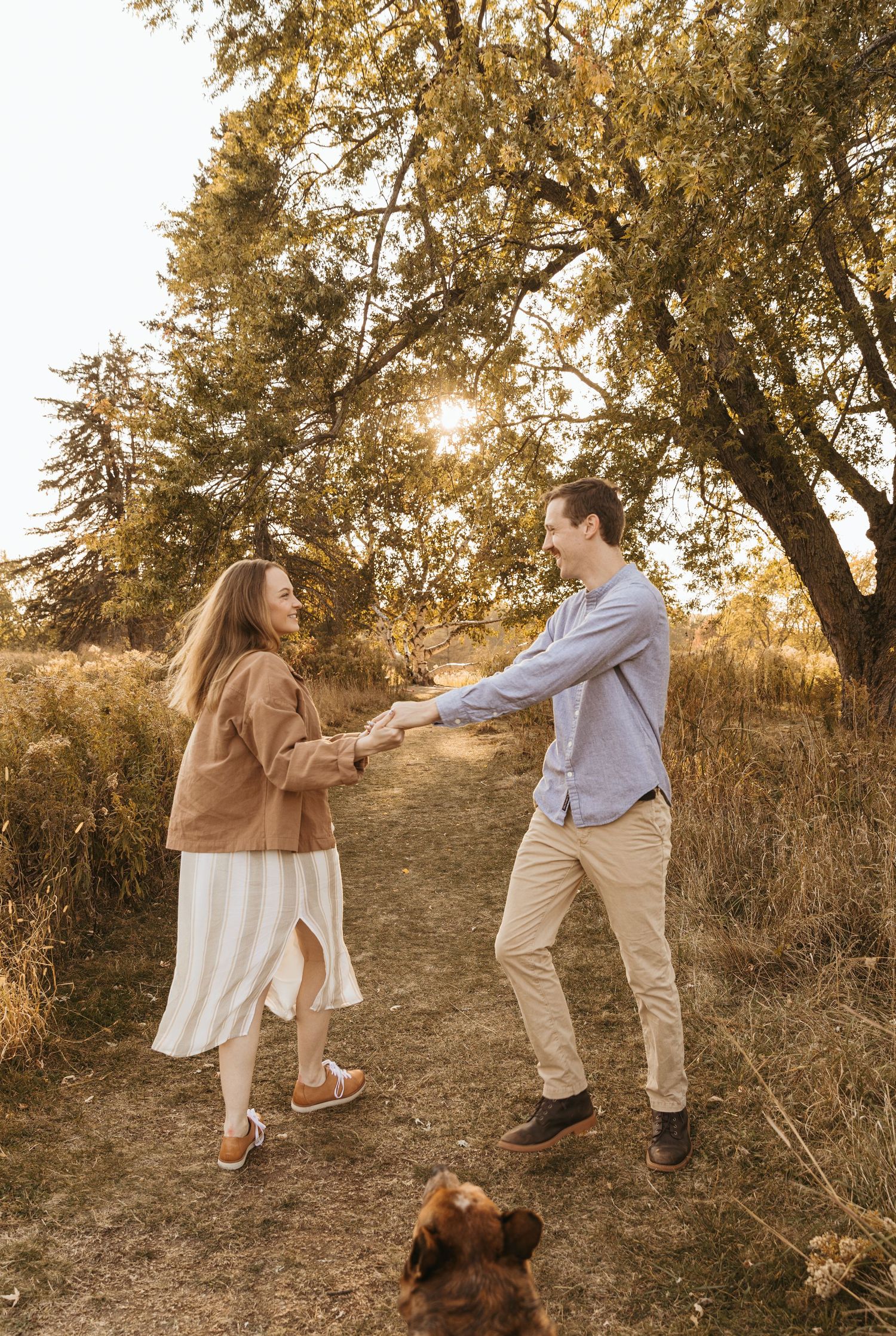 Couple dancing playfully on a trail with their dog watching in the warm autumn light.