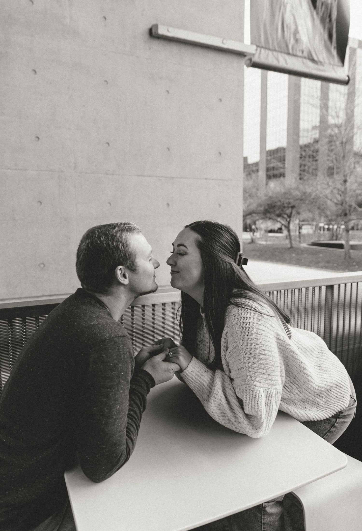 Couple leaning across a white table sharing a tender moment in an outdoor setting.