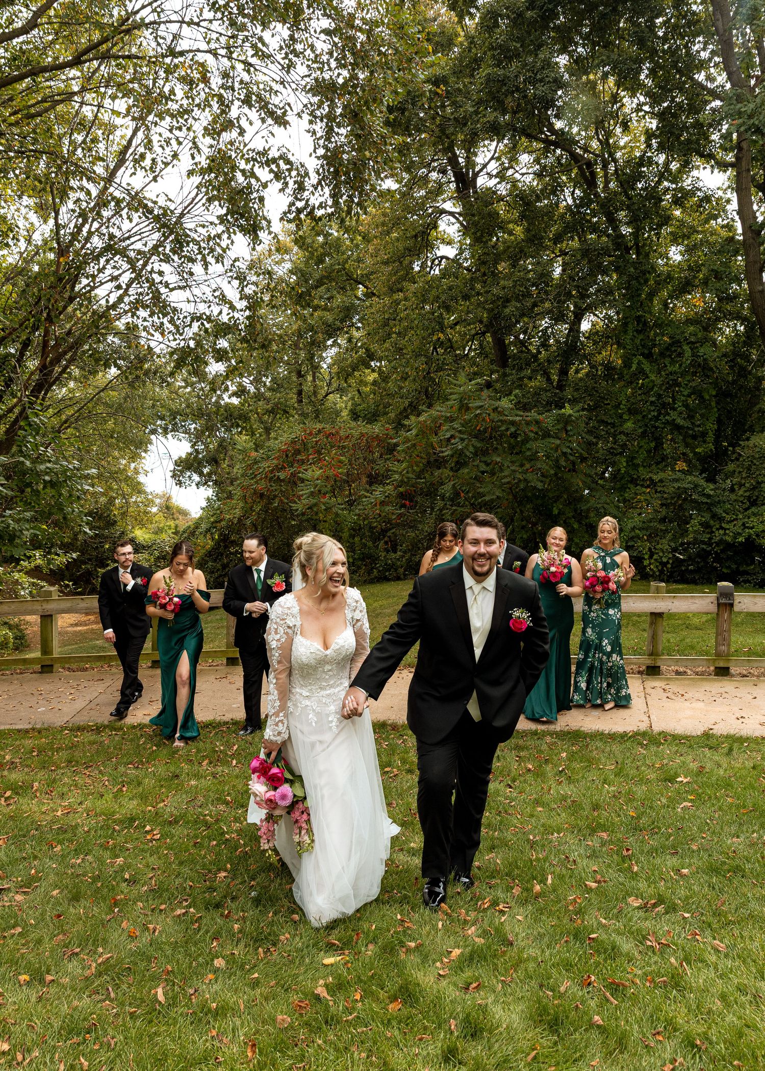 Wedding party walking and celebrating across a grassy field on a sunny autumn day.