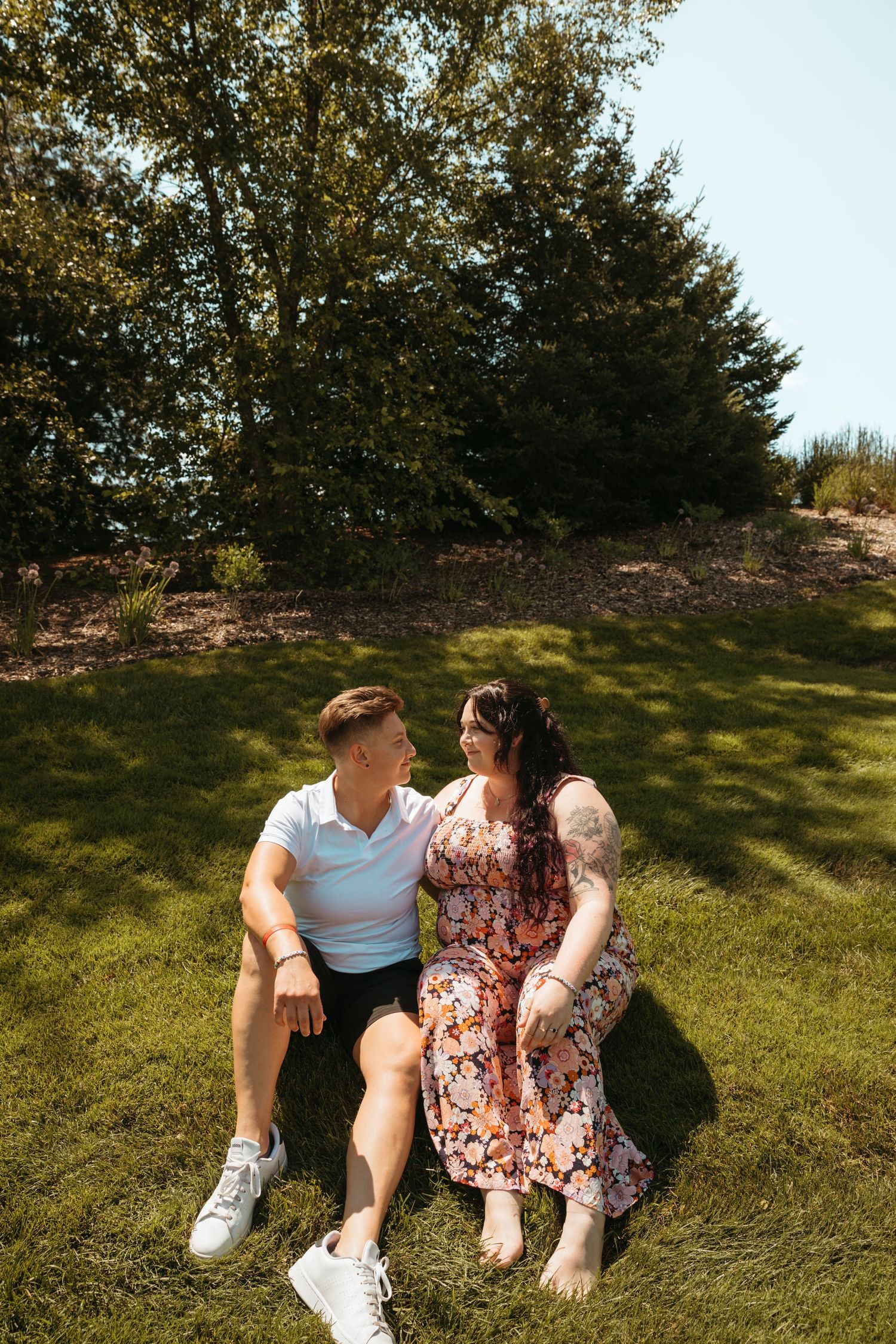 A couple lounges together on a grassy hillside on a sunny day, creating a romantic outdoor moment.