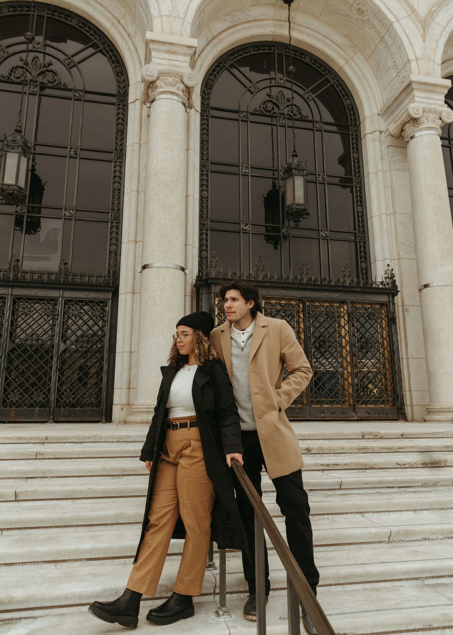 A couple in casual attire lounges on architectural steps with arched columns.