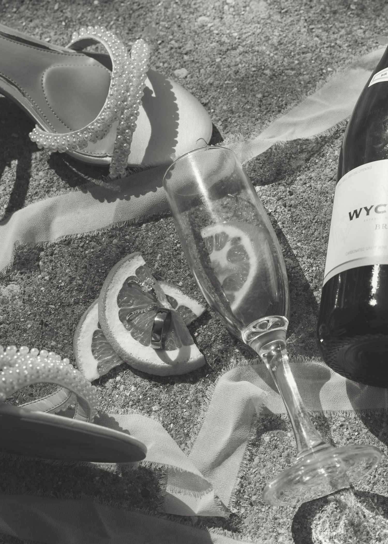 Black and white image of scattered wine glasses and bottles on a textured surface.