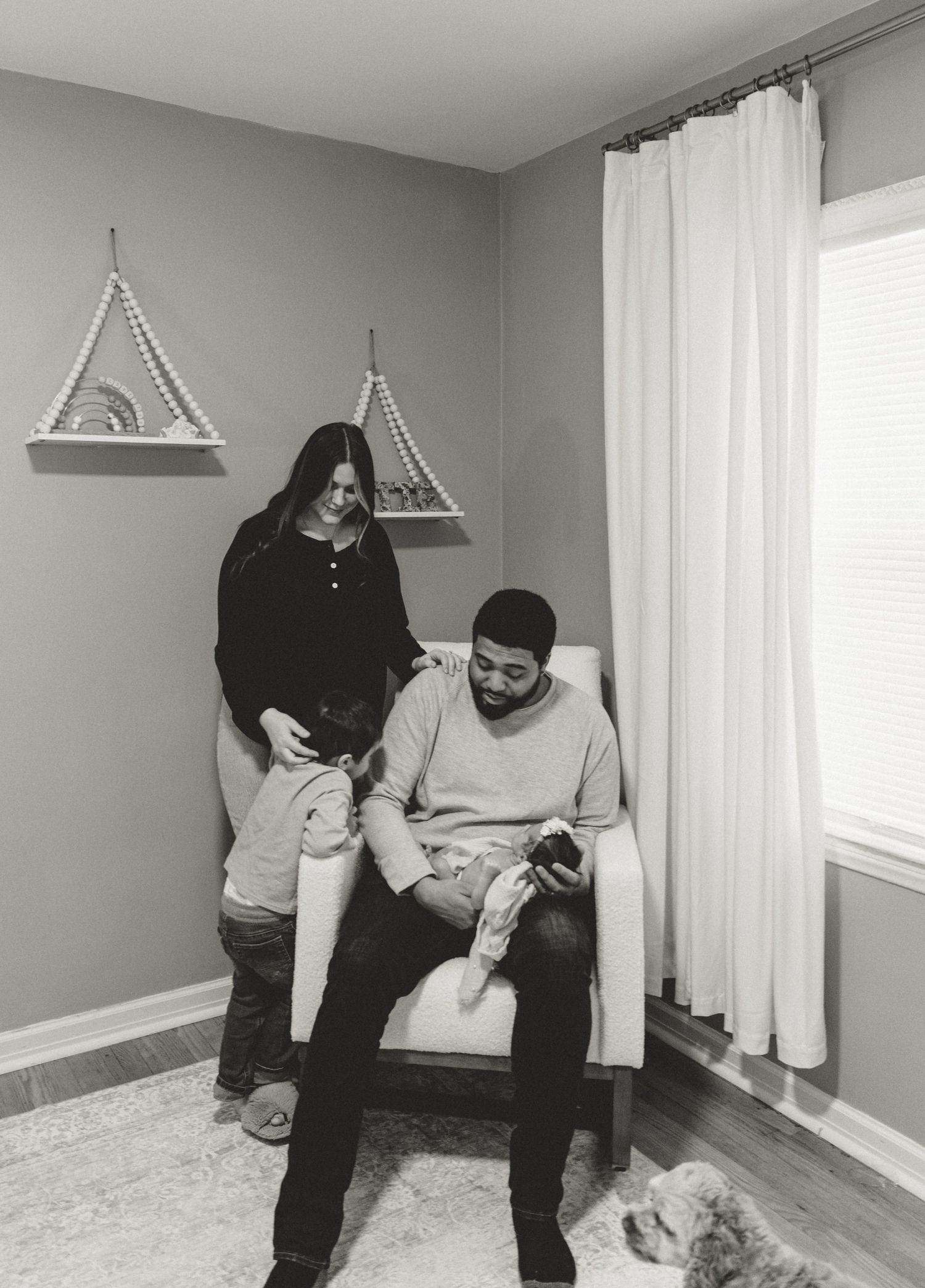 A tender black and white photo series showing a couple holding and gazing at their newborn baby in a bright room.