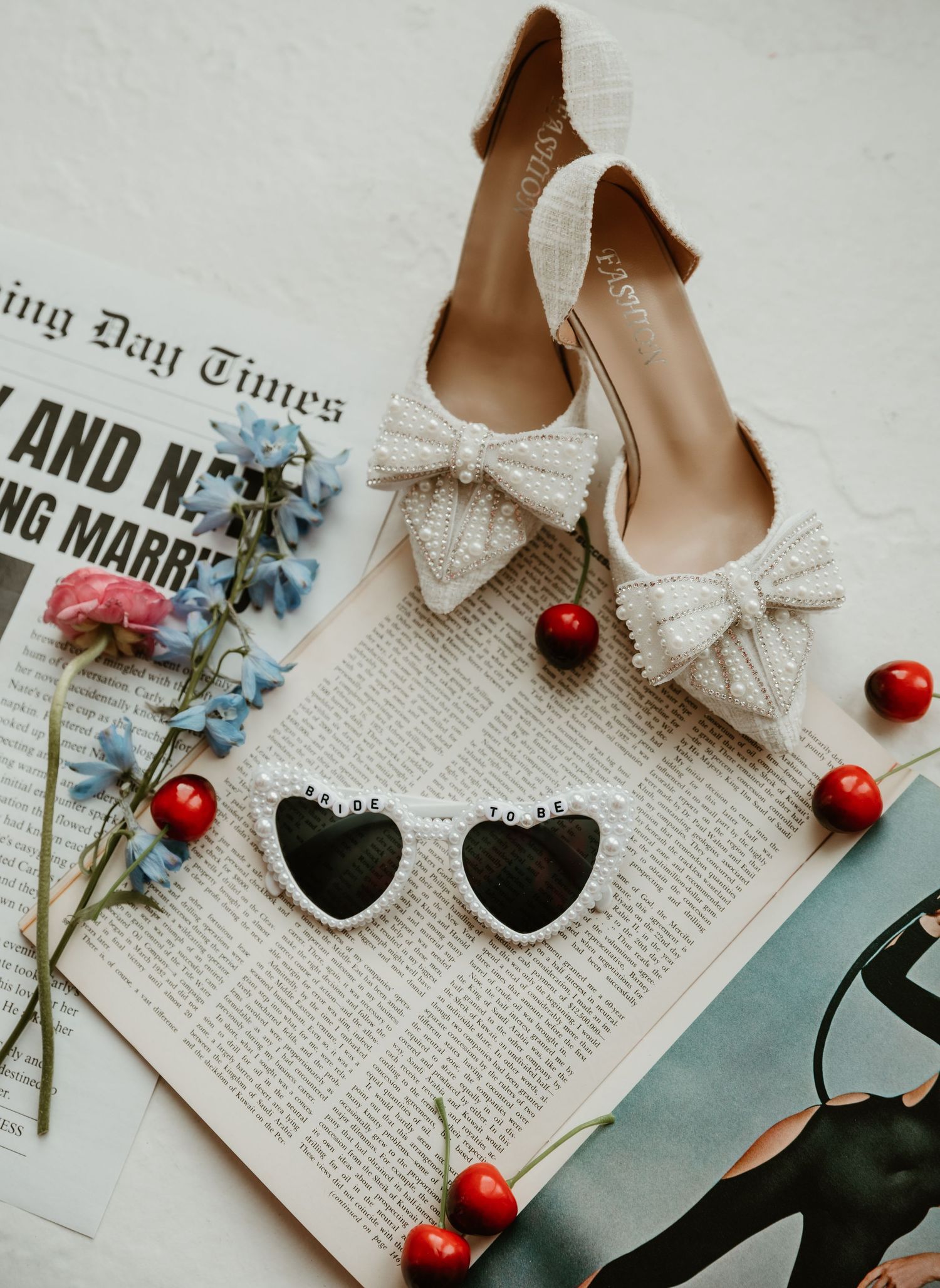 Vintage-inspired wedding detail shot with cherries, heart shoes, and newspaper on light background.