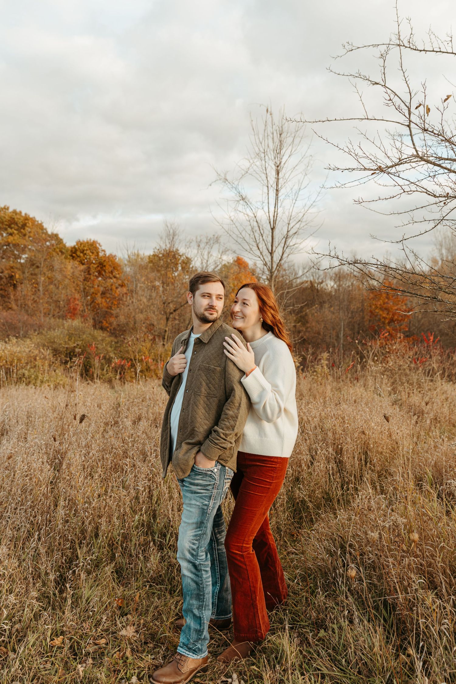 A couple laughs together while standing in a serene autumn meadow.