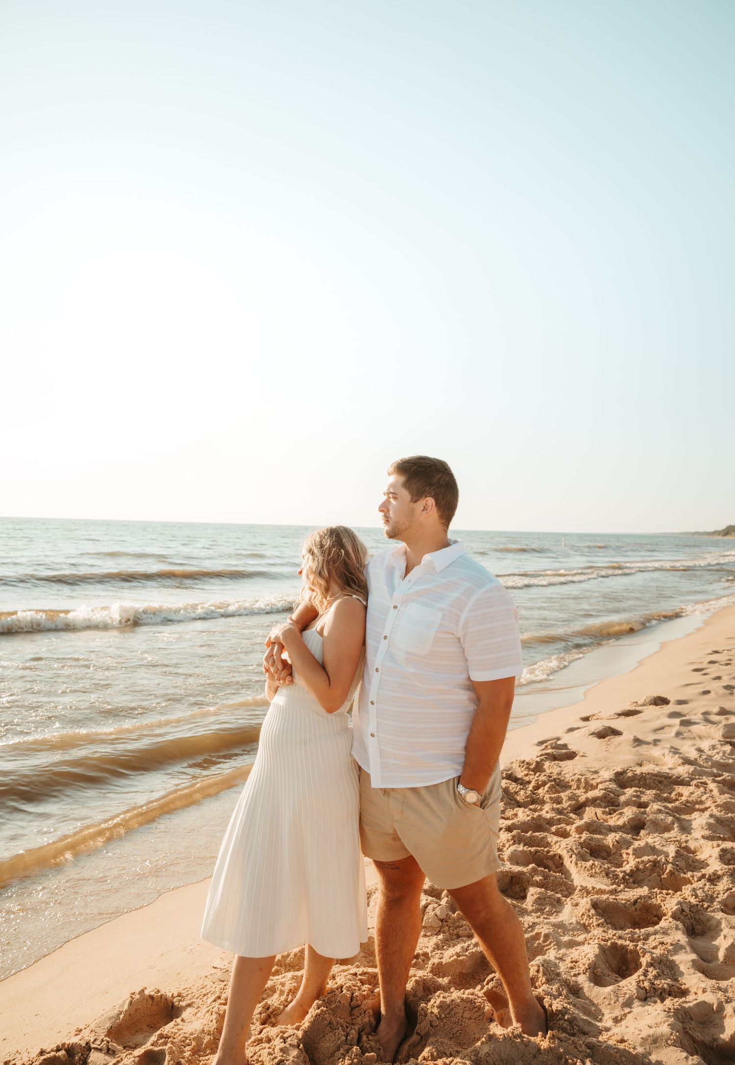 Couple in white outfits sharing playful moment on beach at sunset.