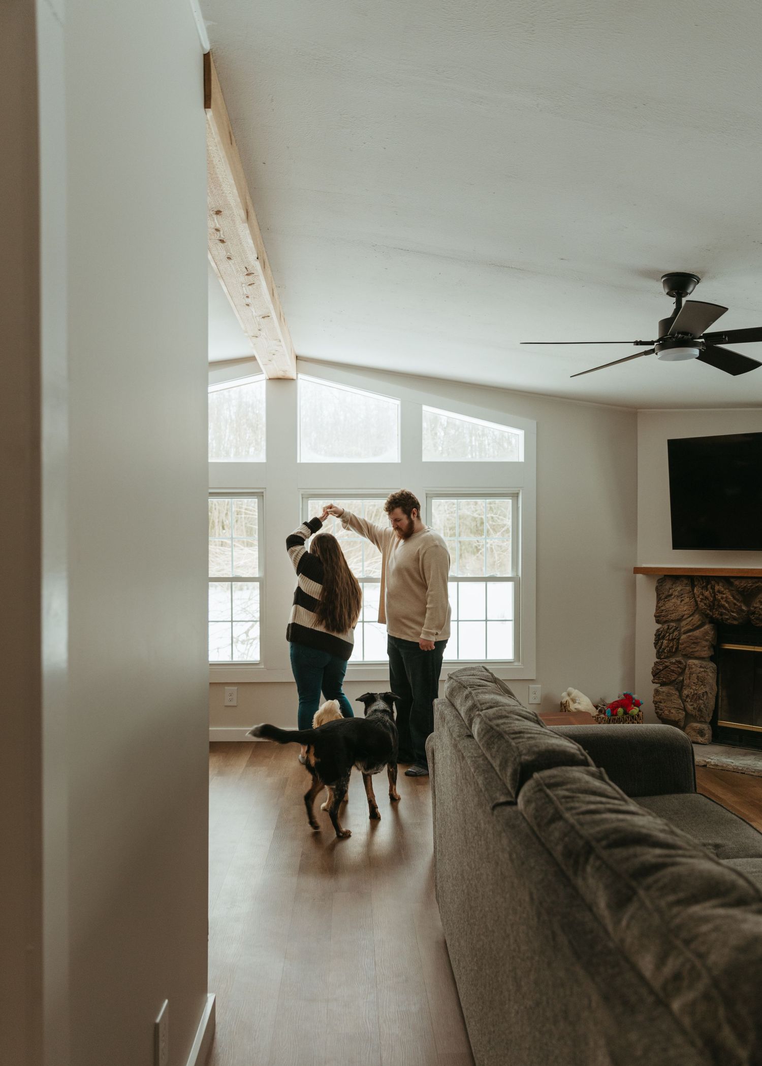 A couple dances together in a bright, modern living room with large windows.