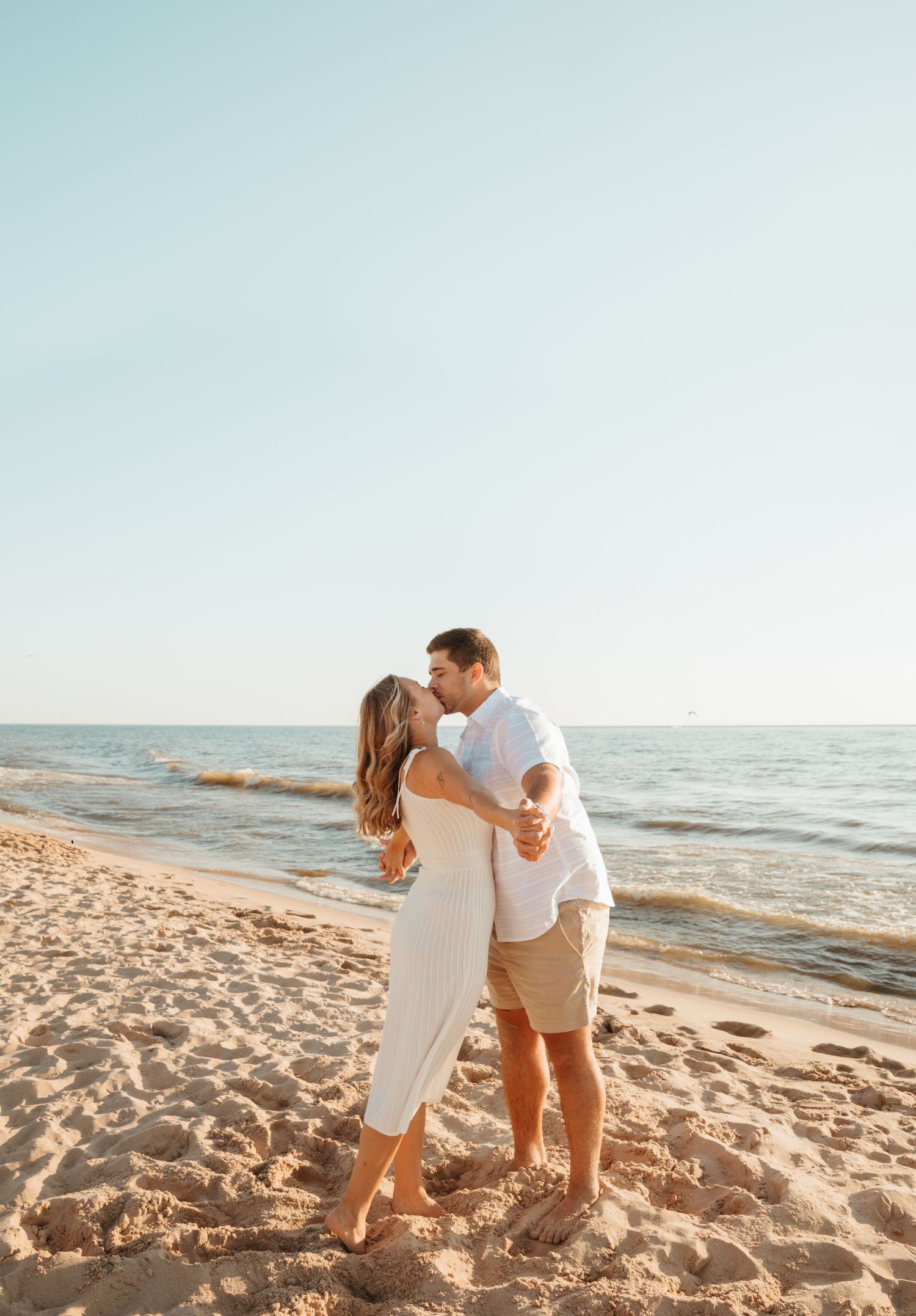 Couple embracing on sandy beach with ocean waves in background during golden hour.