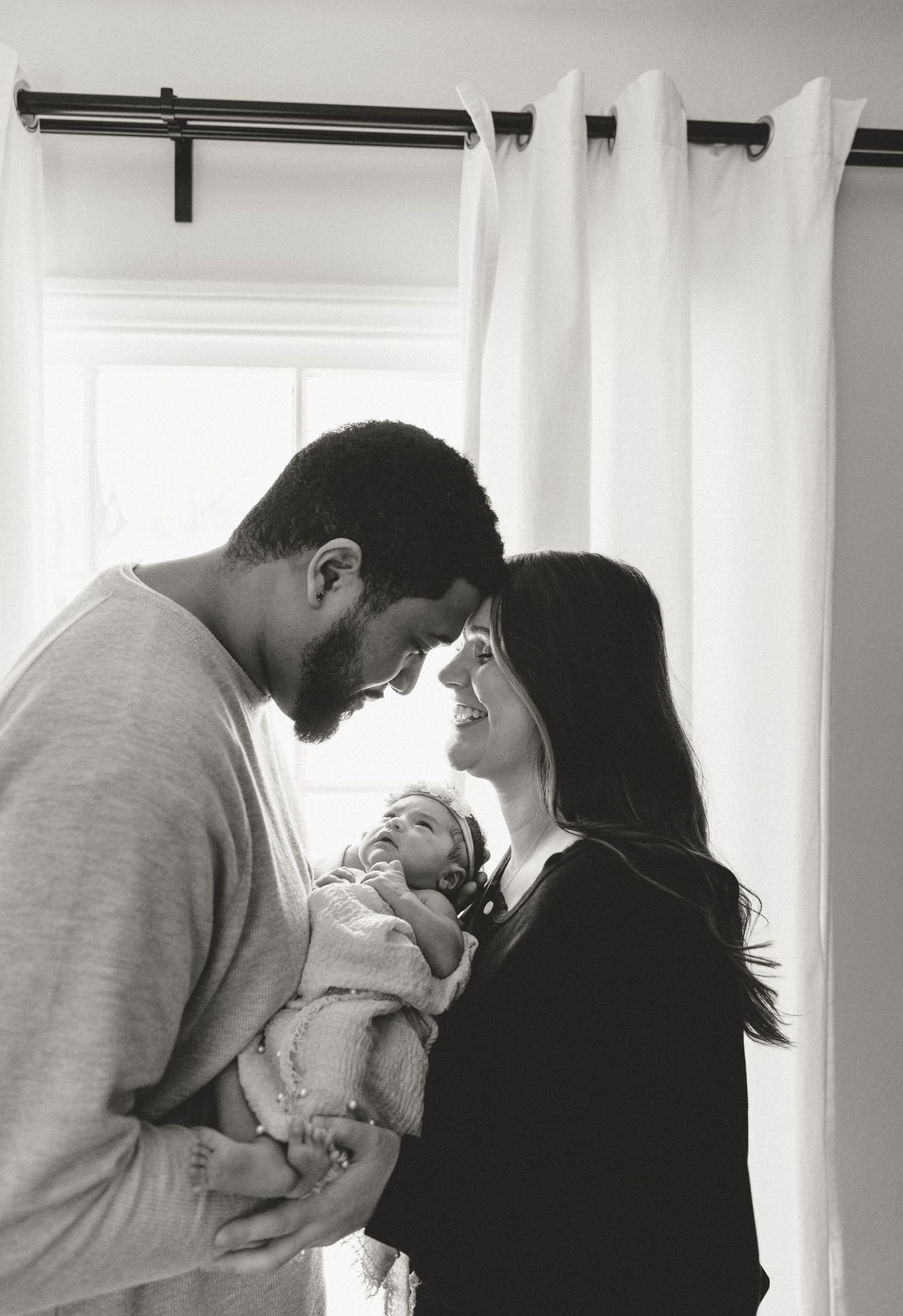 Black and white series capturing tender moments between parents and their newborn by a window.