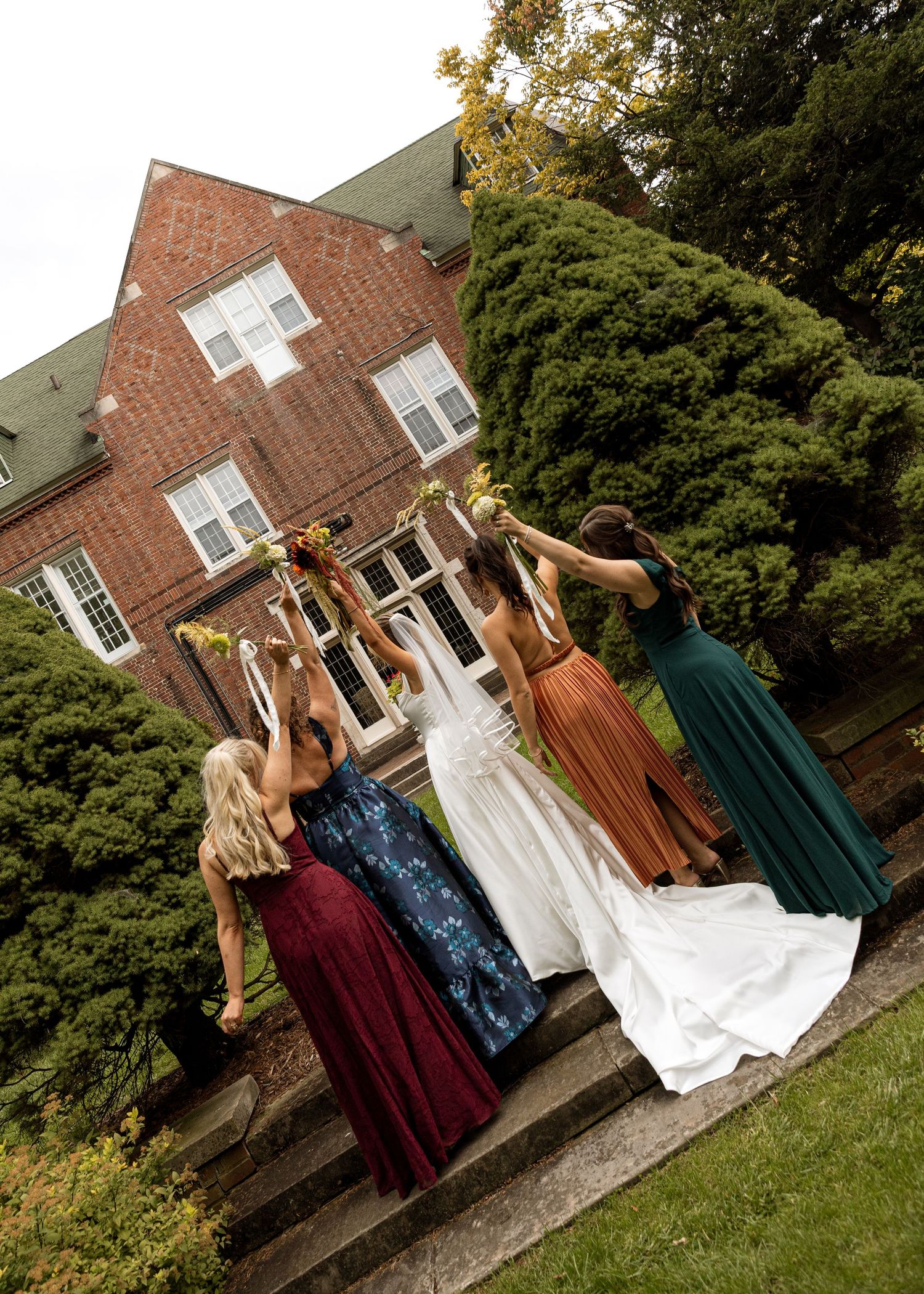 Wedding party in colorful dresses poses playfully outside a brick building.