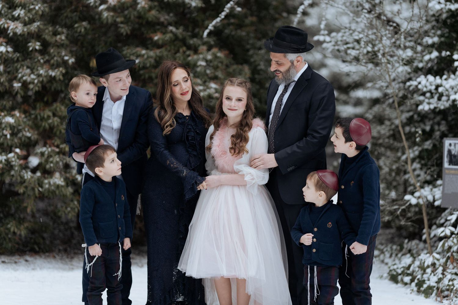 A formal winter family portrait with snow-covered trees in the background.