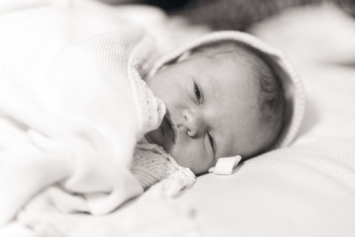 A sleeping baby wrapped in soft white blankets in black and white.