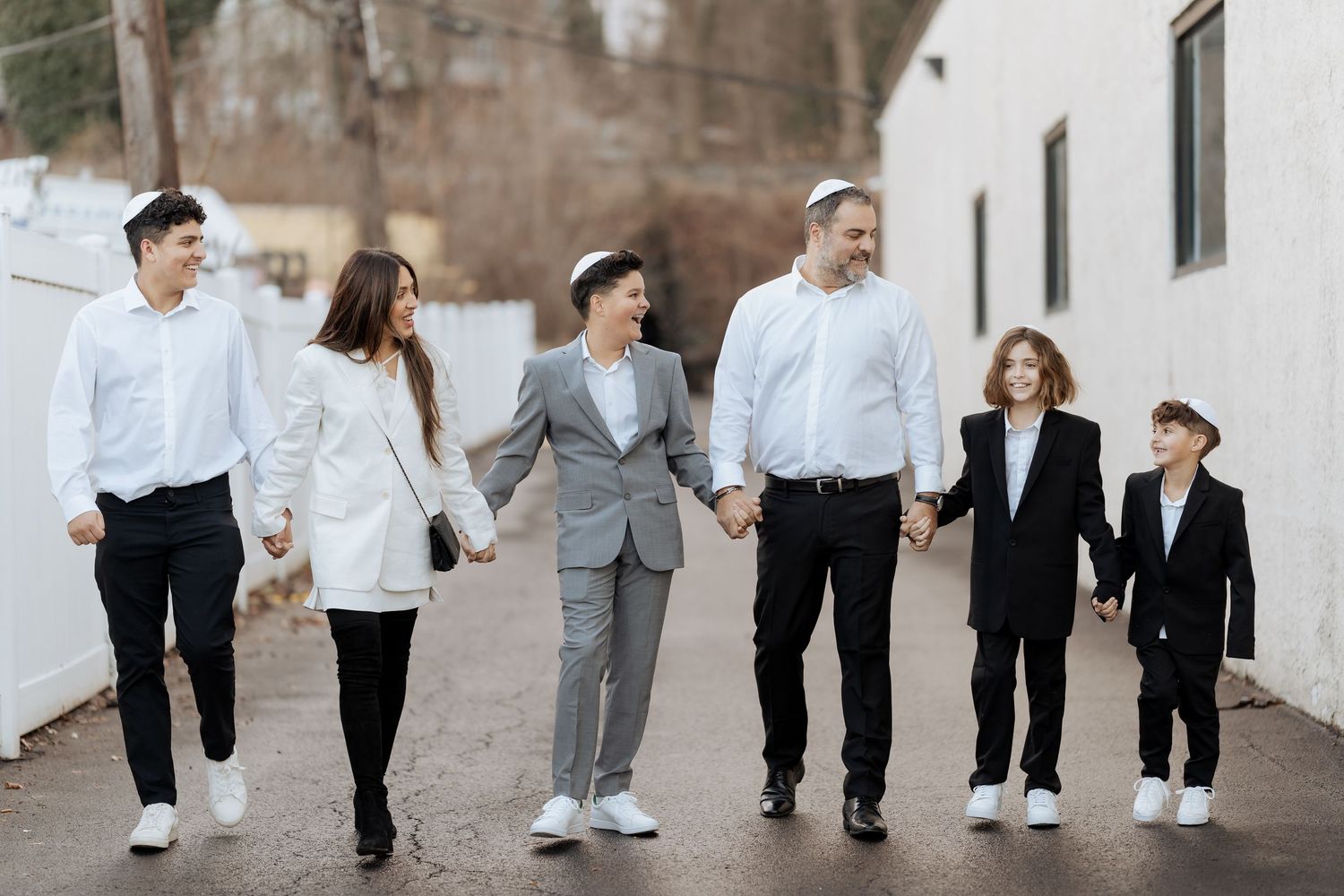 A group walking together holding hands outdoors against a white wall.