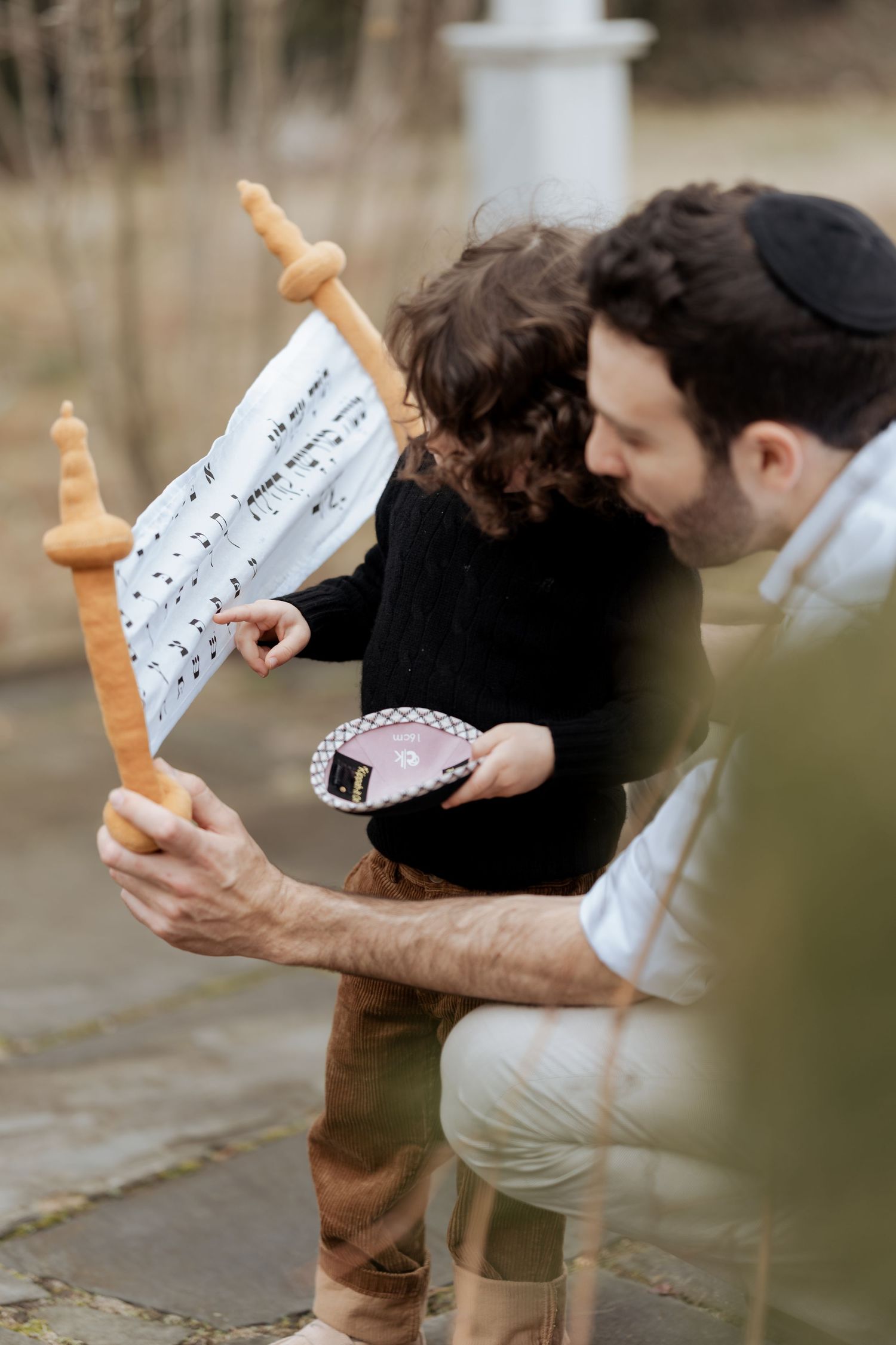 A person wearing a yarmulke examines a Torah scroll outdoors.