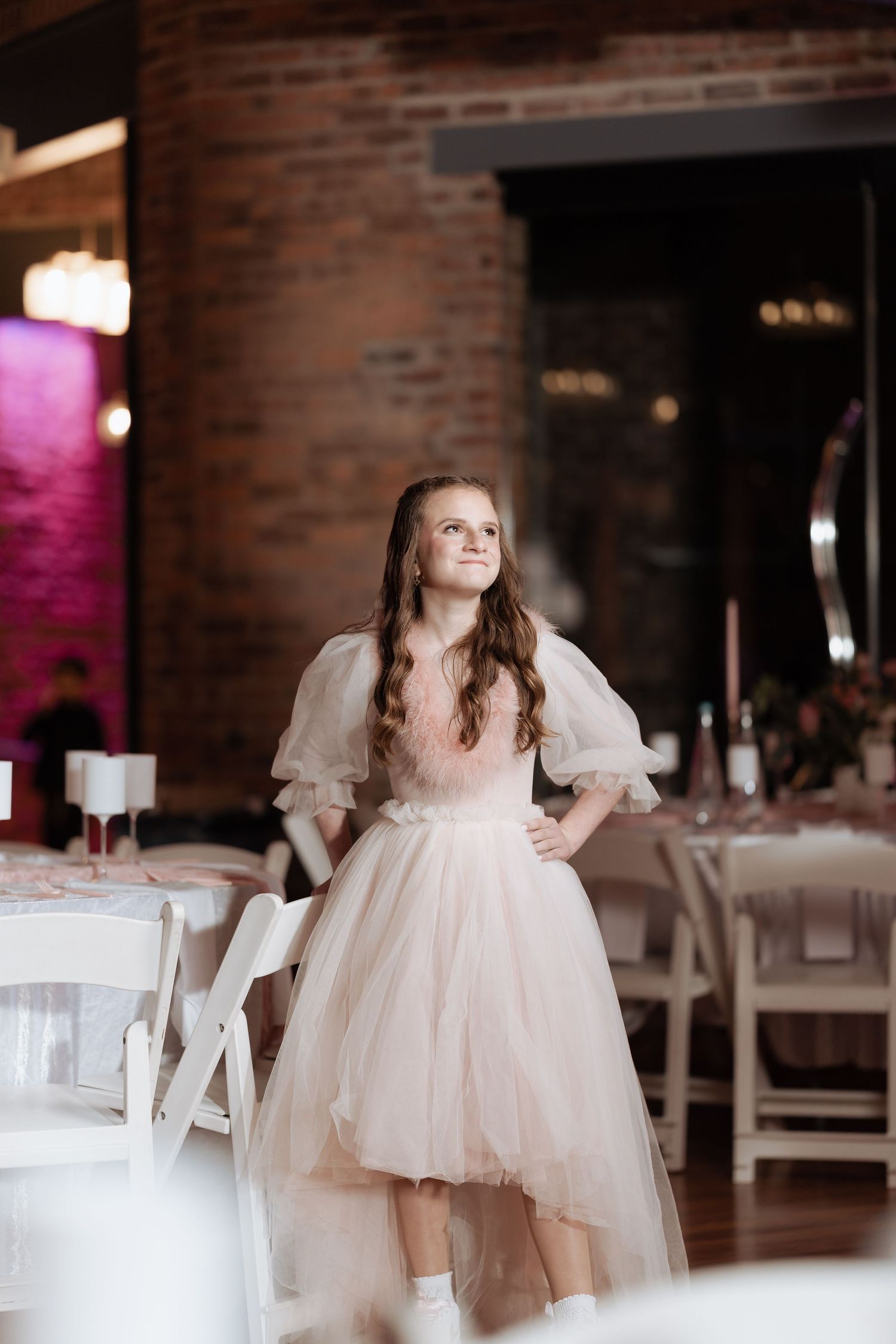 A dreamy portrait in a brick venue featuring a romantic blush tulle dress with puff sleeves.