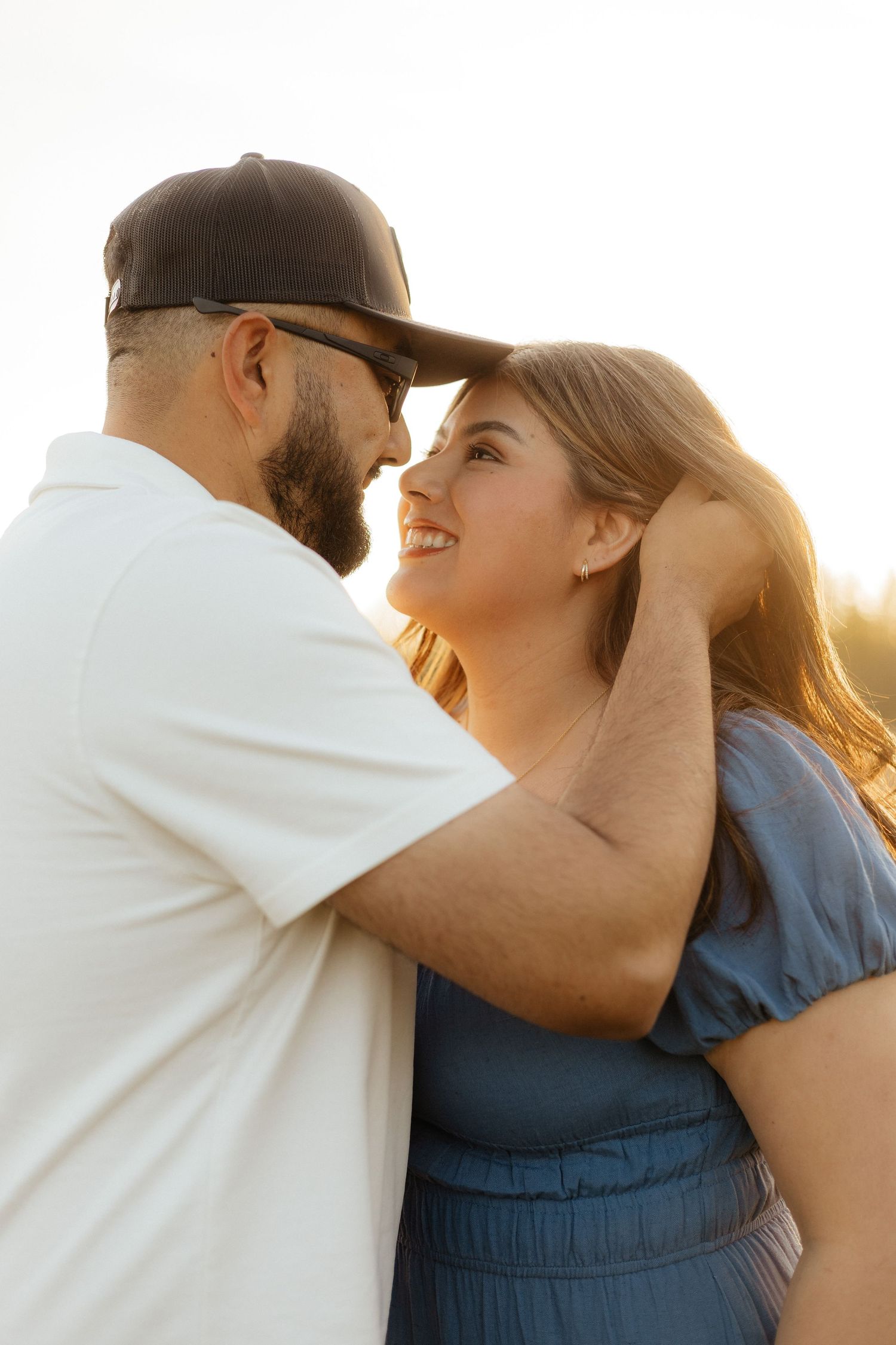 Couple sharing an intimate moment in warm sunlight as they smile at each other outdoors.
