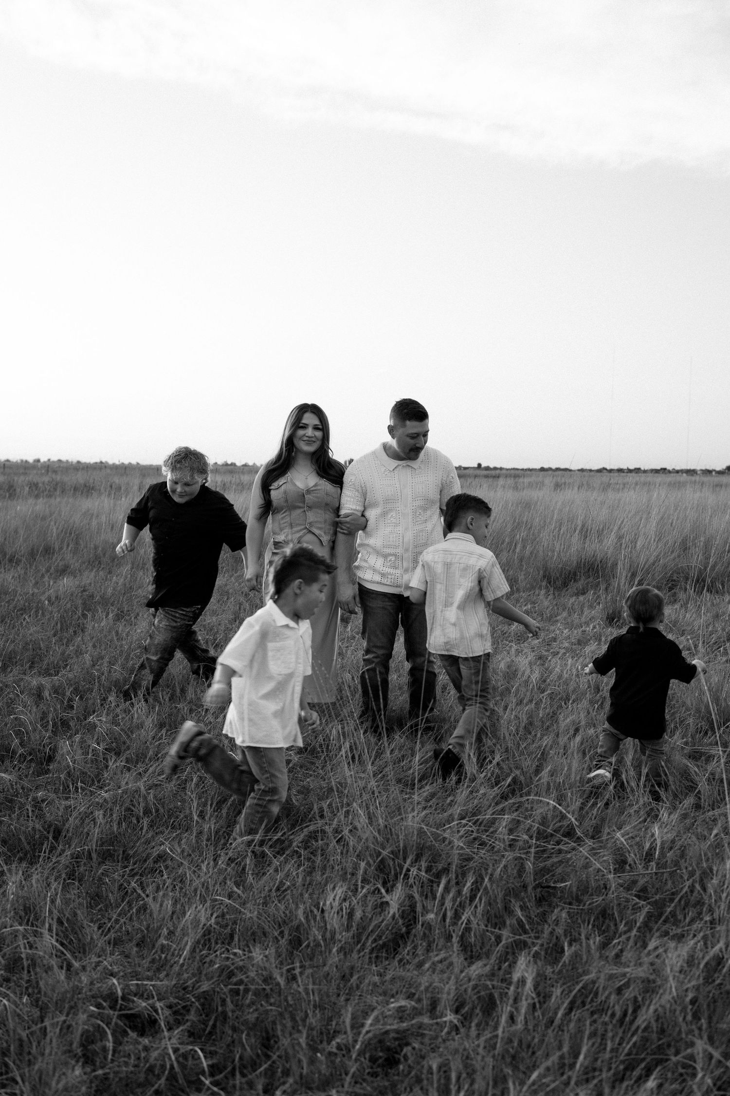 Family walking together through a tall grass field in black and white photography.