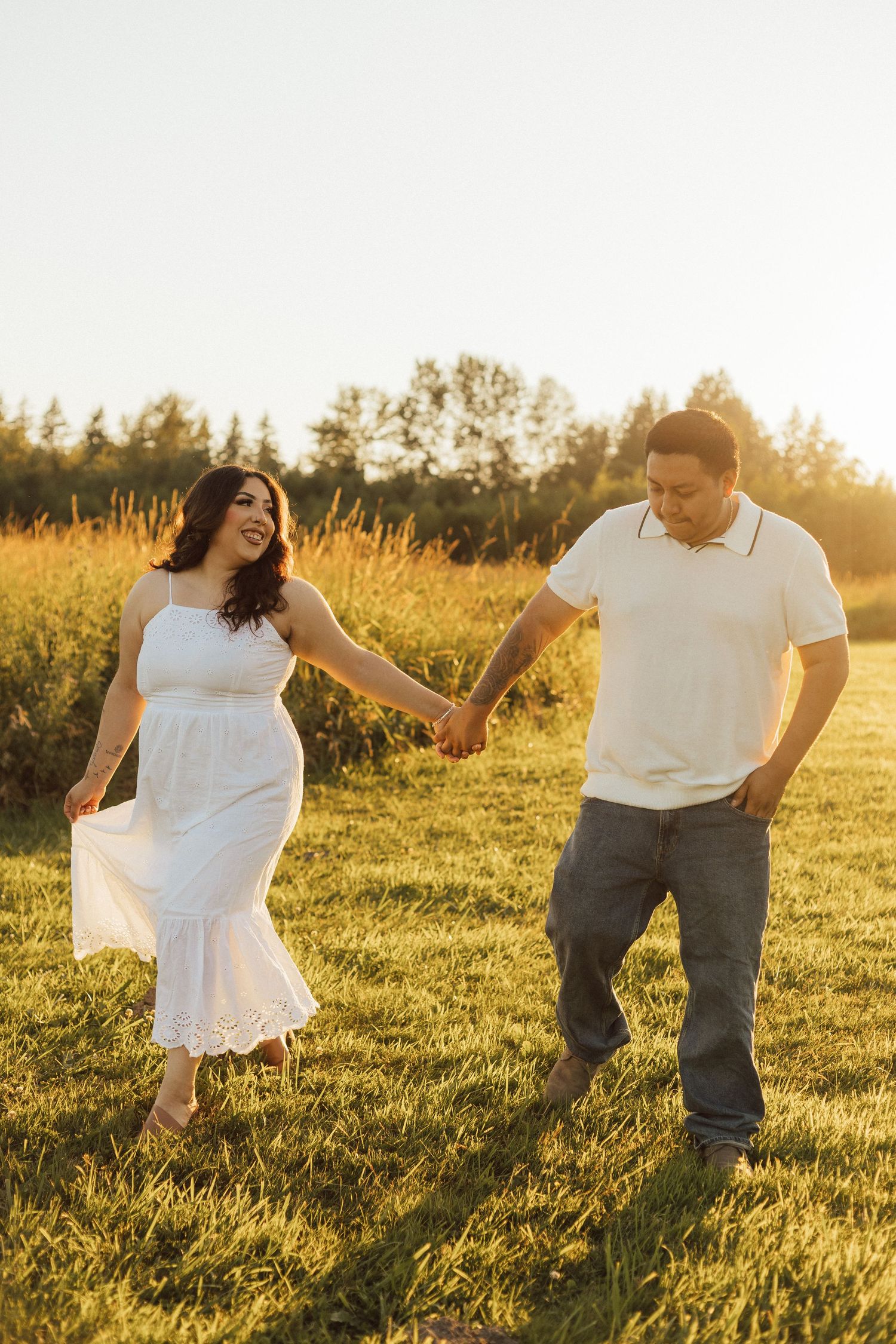 Couple enjoying a romantic moment in a sunlit meadow at golden hour, with the woman wearing a flowing white dress.
