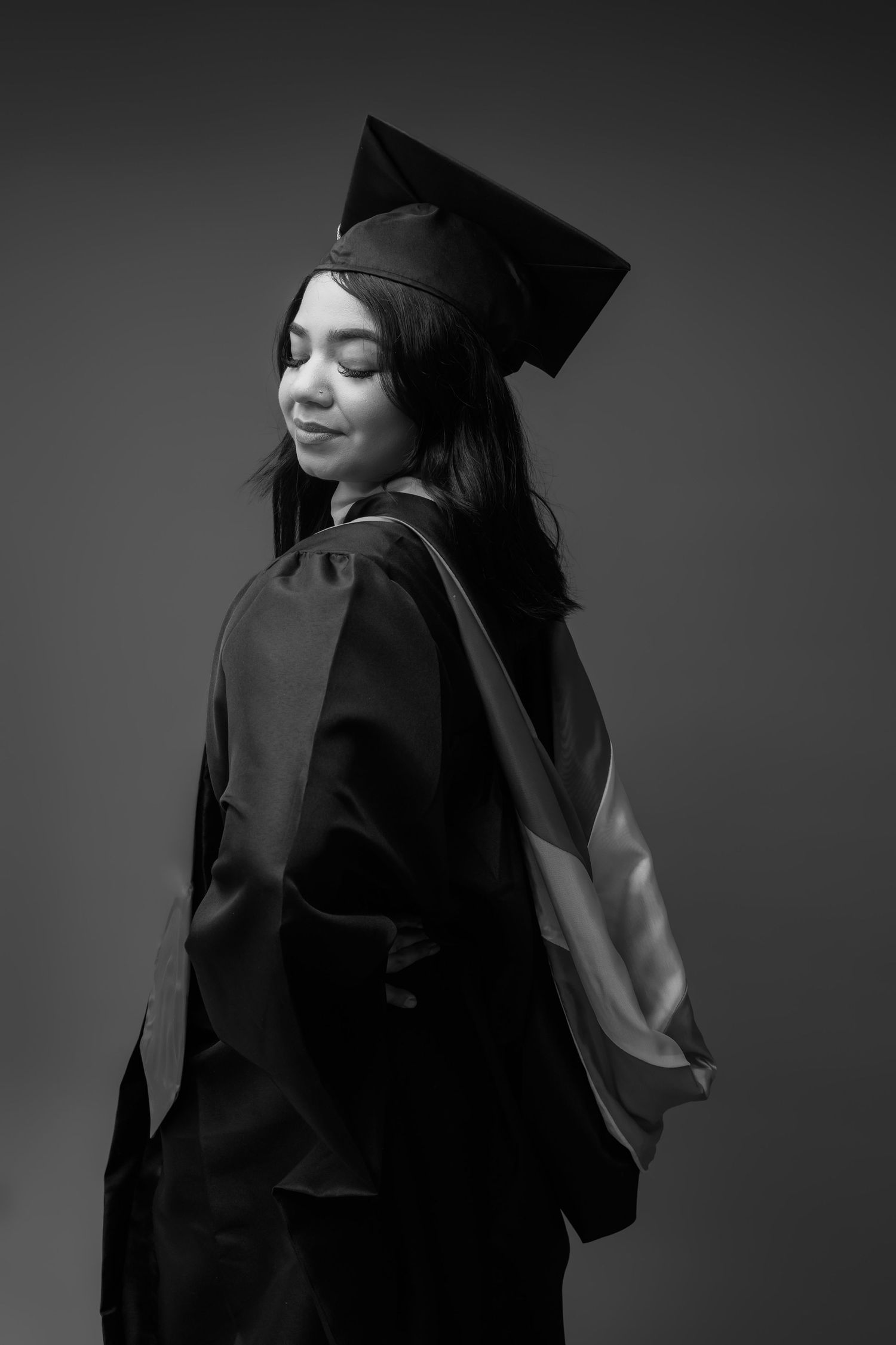 A black and white series shows a figure in graduation attire turning to different angles with shadows and contrast.