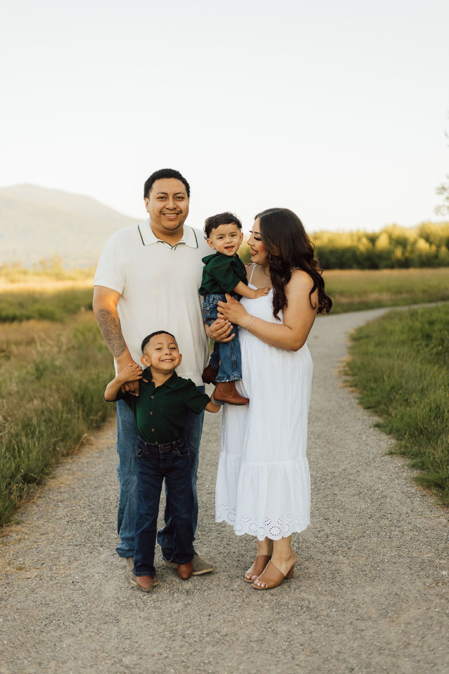 A family stands together on a dirt path during golden hour with mountains visible in the background.