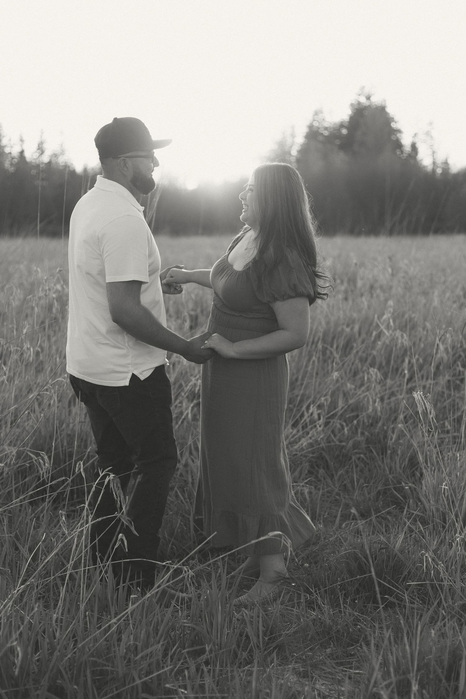 A couple stands holding each other in a field at sunset, silhouetted against the glowing late day light.