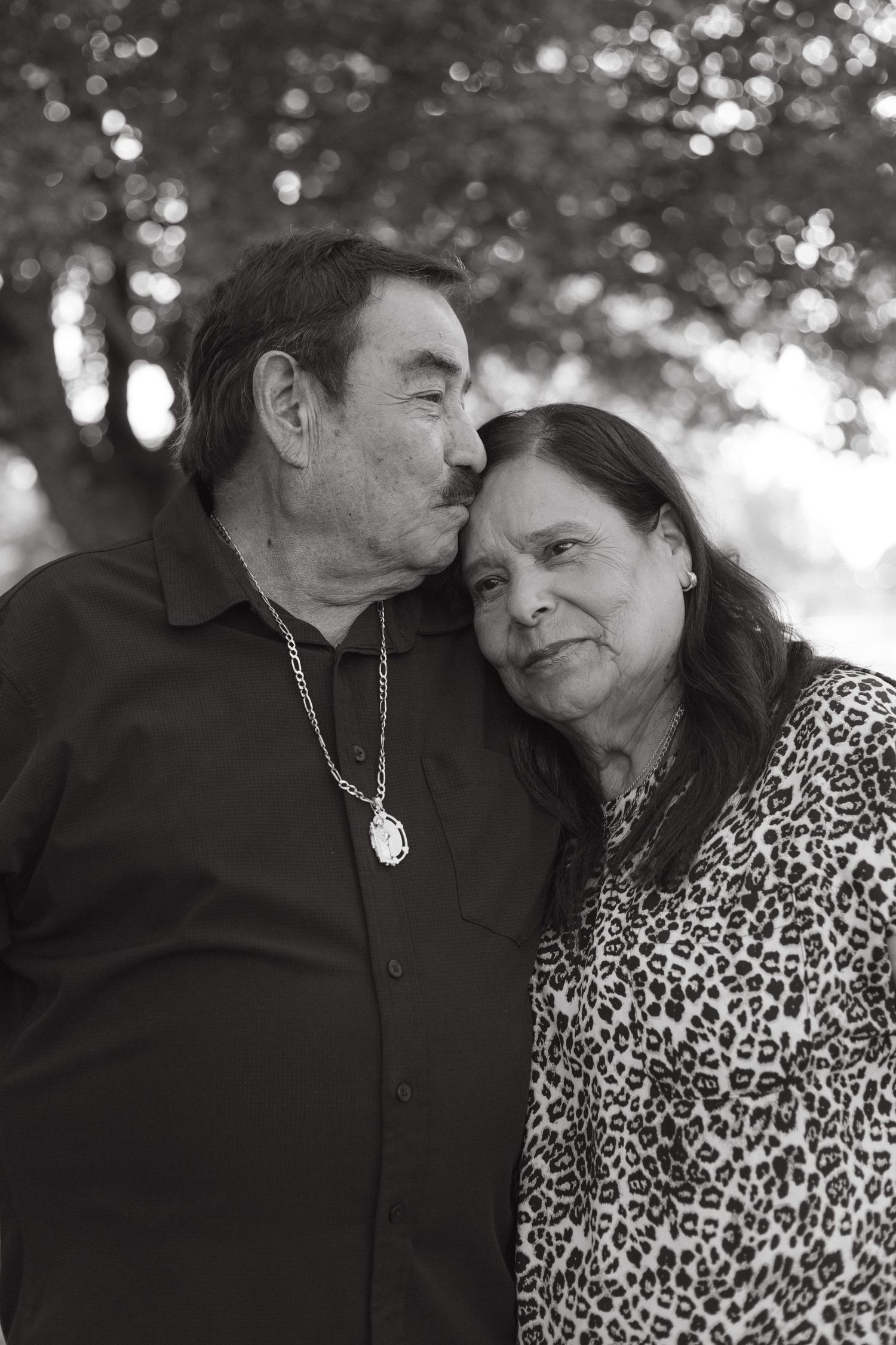 Black and white photo series showing an intimate couple in casual clothing embracing tenderly against a bokeh background.
