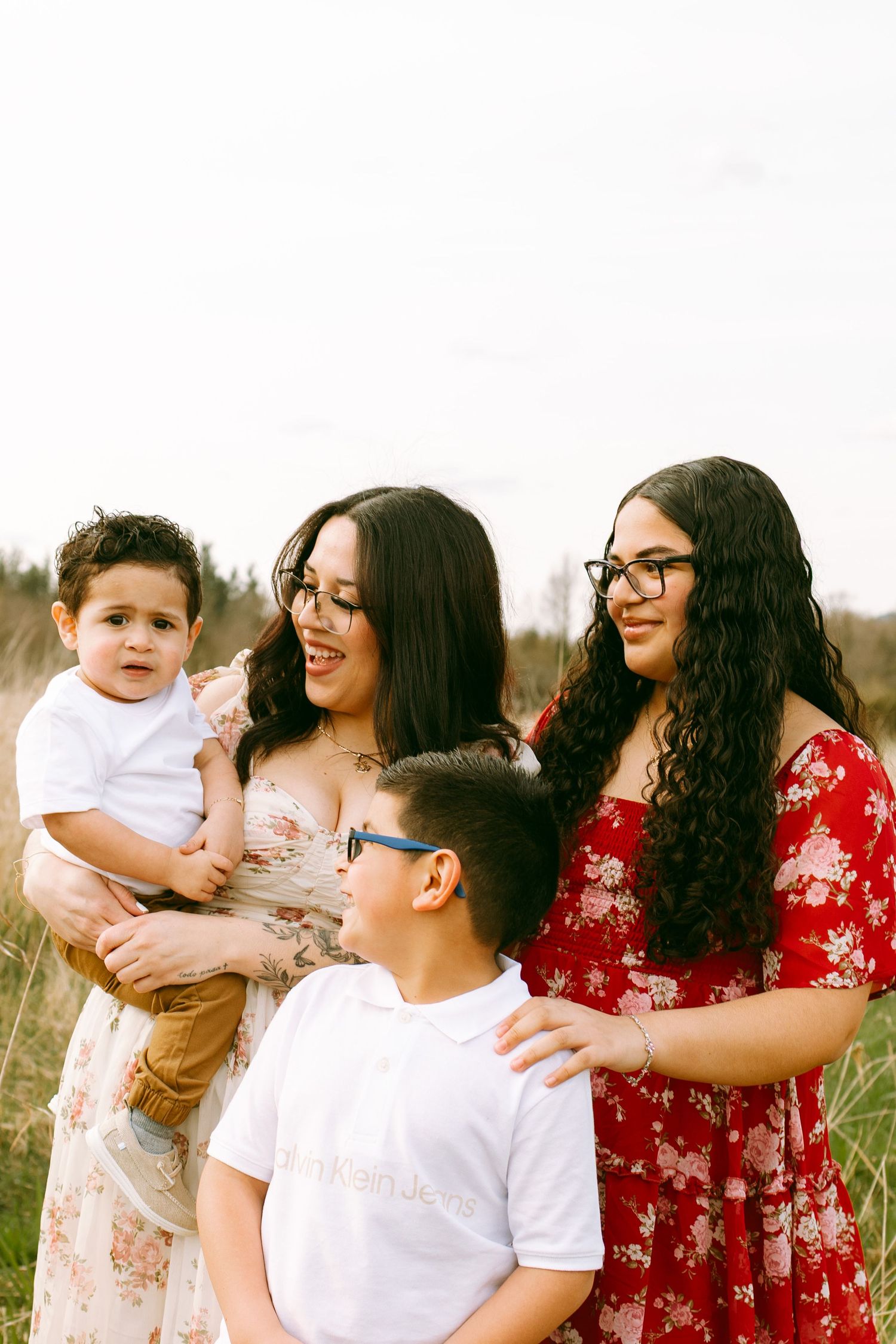 A family group poses together outdoors in a field wearing coordinated outfits of white and floral prints.