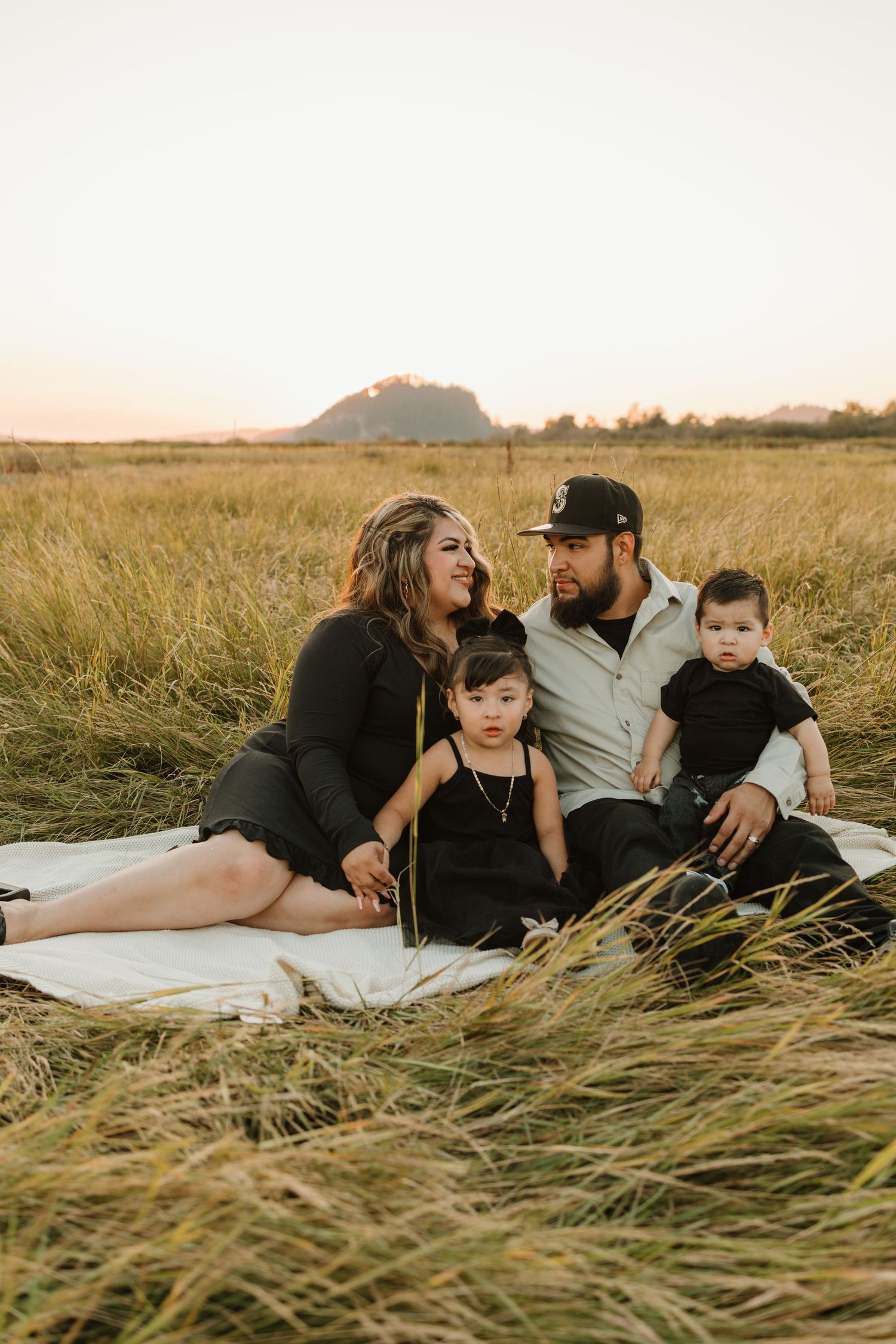 Family sitting together on blanket in tall grass field during golden hour.