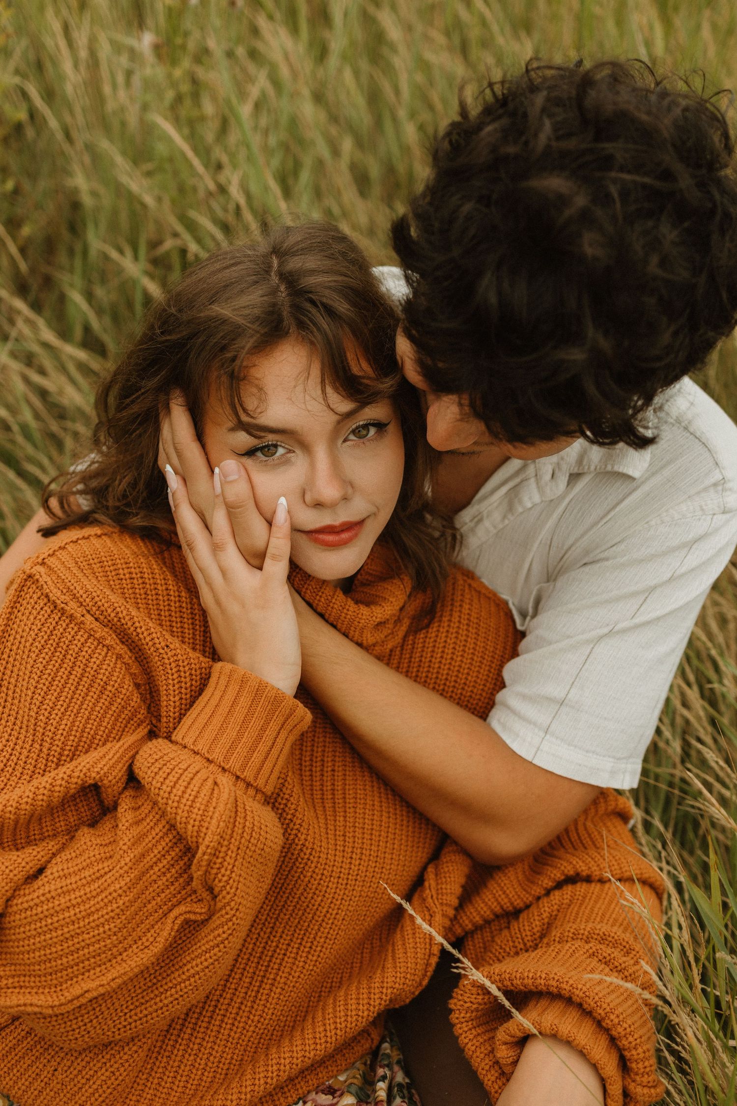 Intimate couple moment in tall grass wearing autumn sweaters.