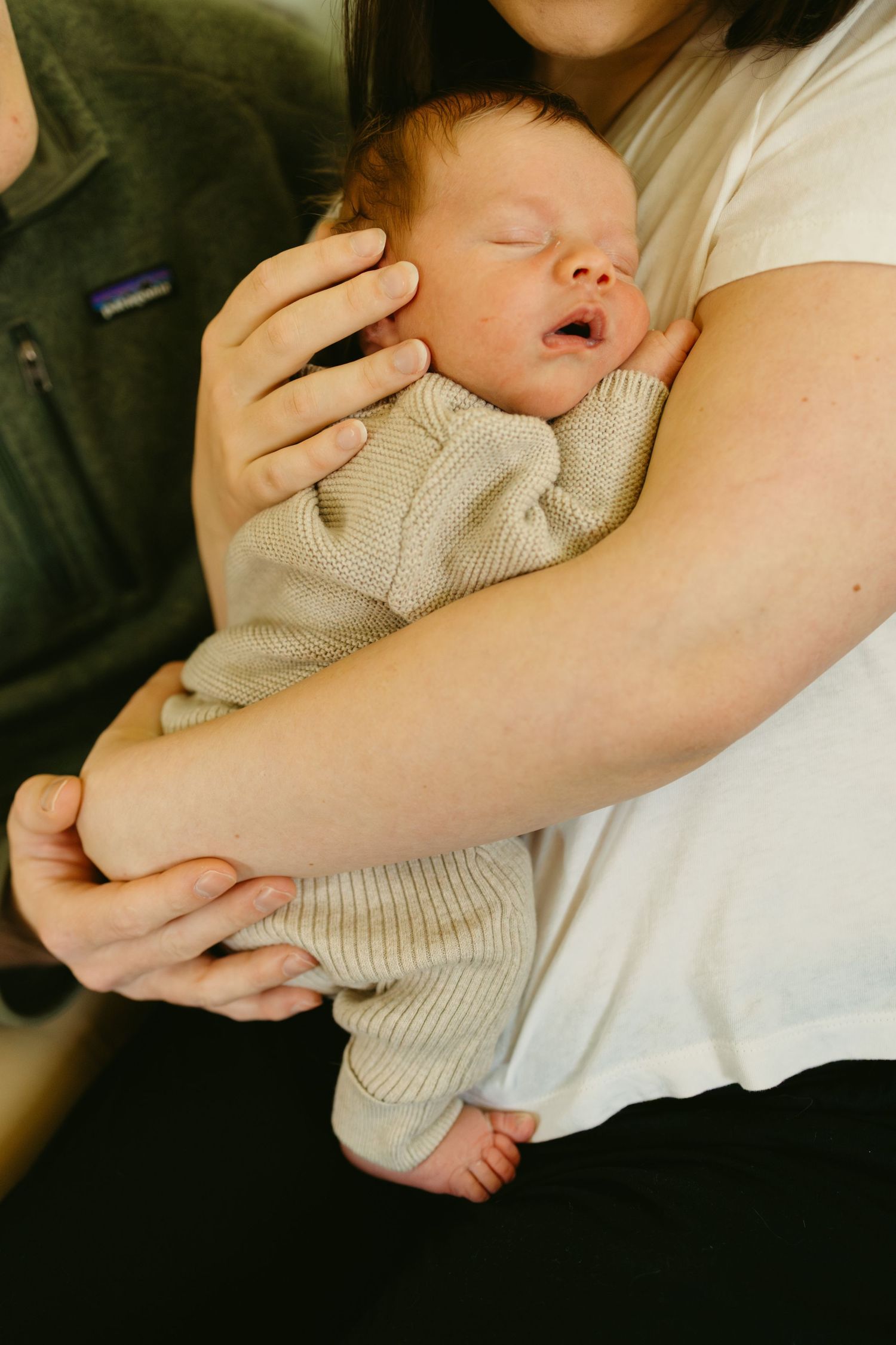 A sleeping newborn baby in a beige knit sweater is cradled in loving arms.