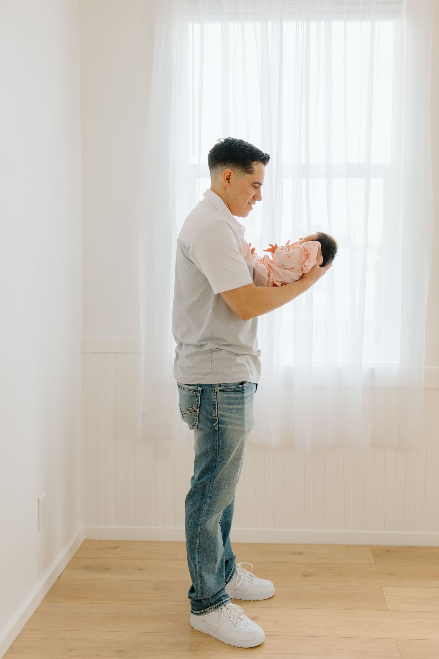 Parent holding newborn baby in bright white room next to window.