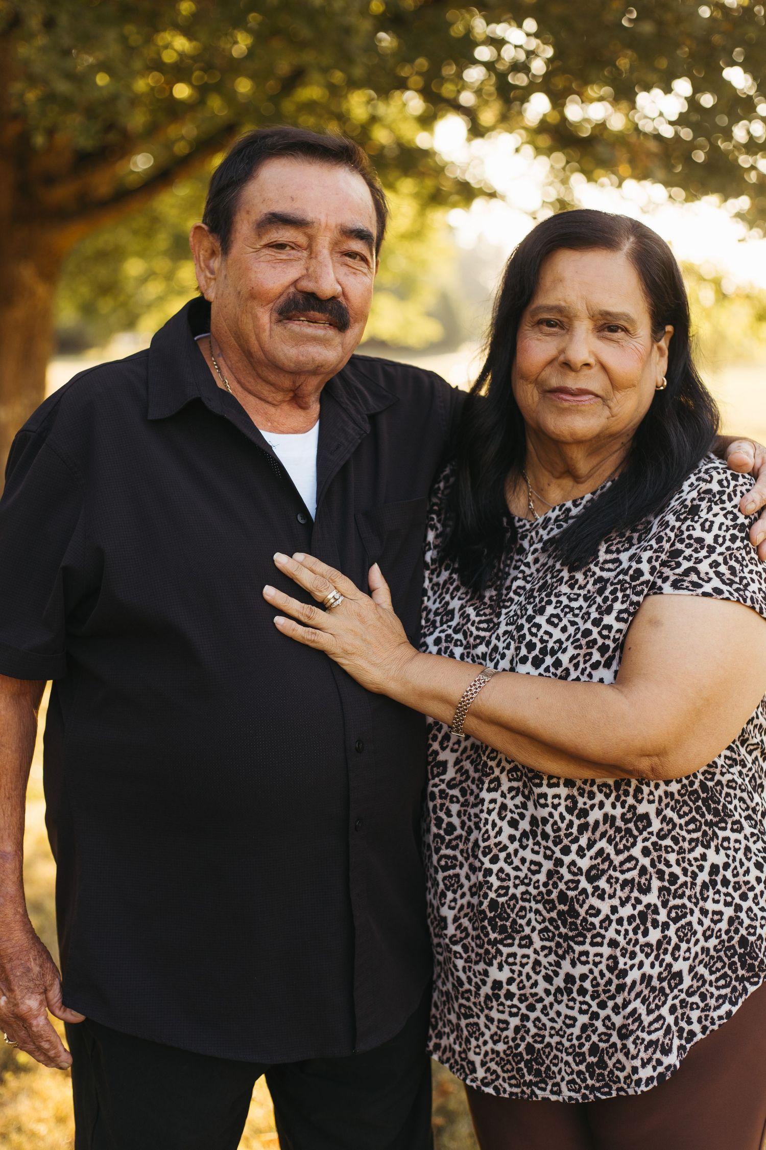 A couple standing together outdoors in warm lighting wearing a black shirt and leopard print blouse.
