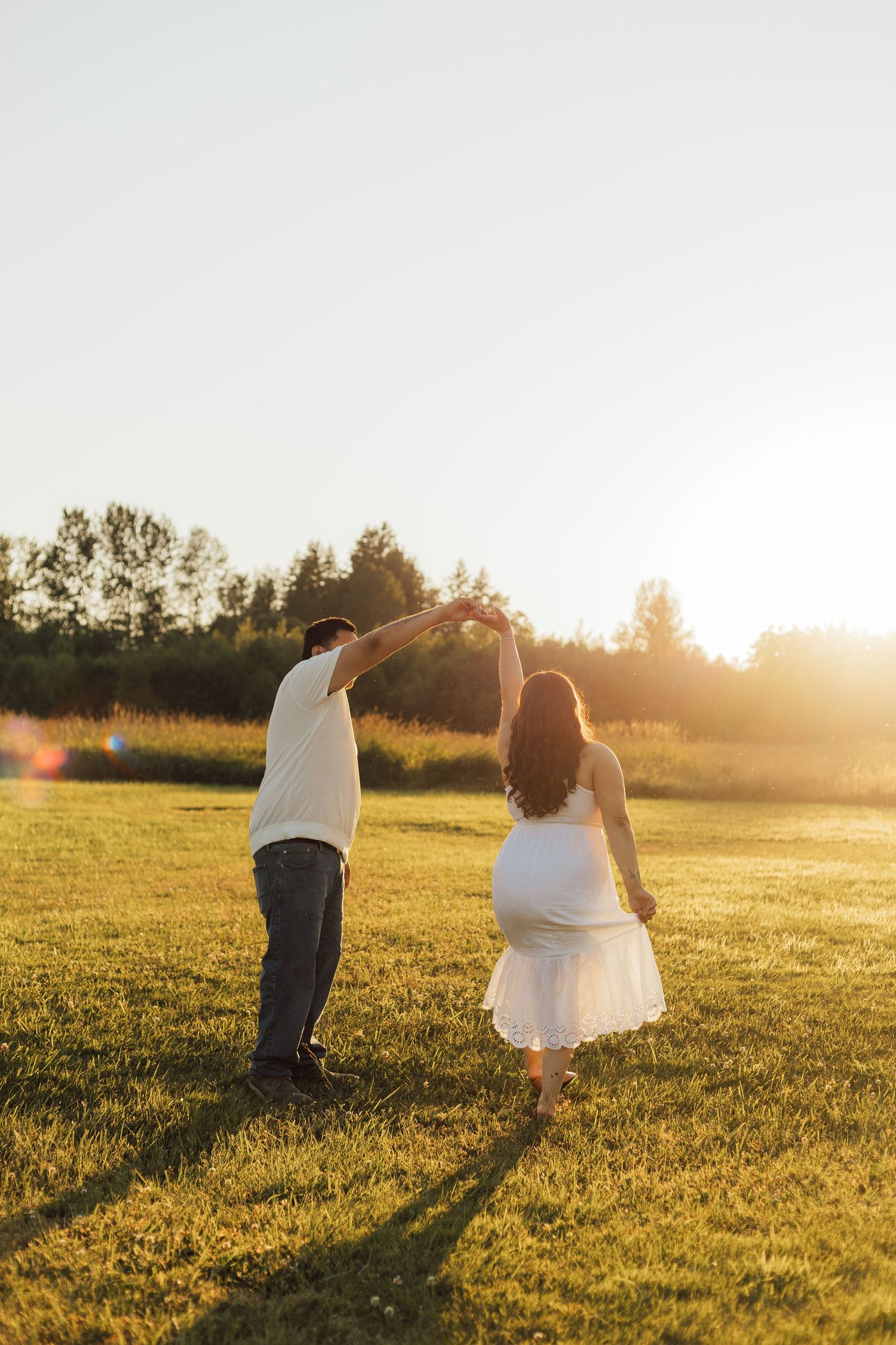 A couple dances together in a sunlit meadow at golden hour, casting long shadows across the grass.