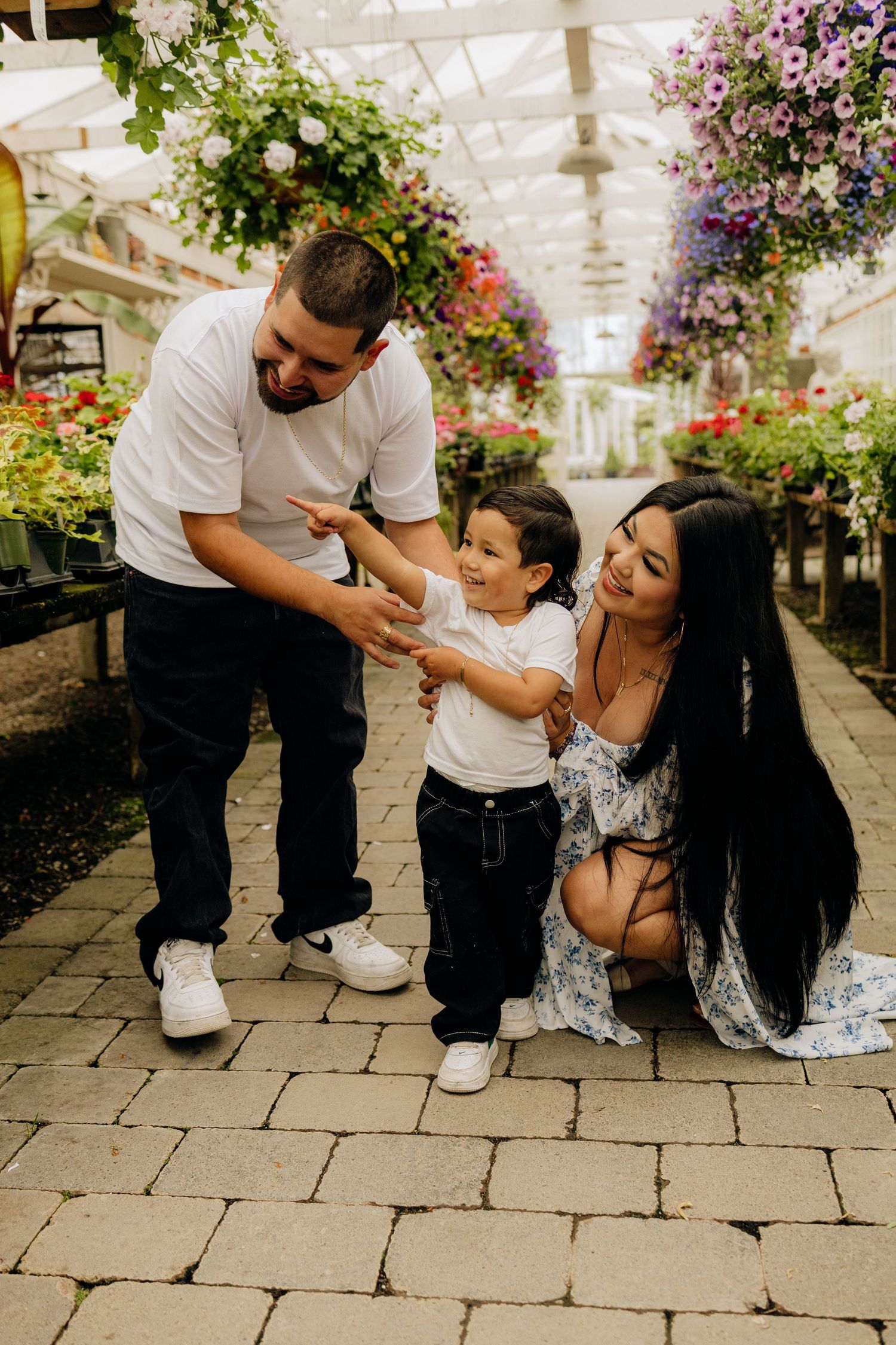 A family shares a joyful moment together in a greenhouse filled with colorful hanging flowers and plants.