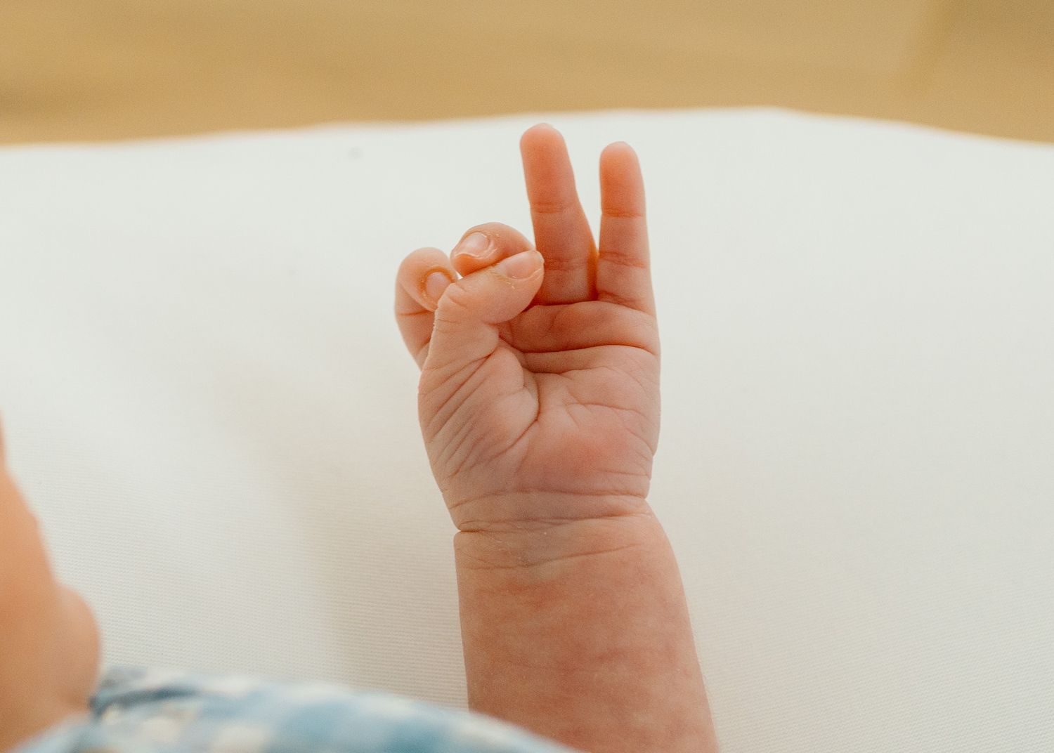 Tiny baby hand showing peace sign gesture against soft white background.