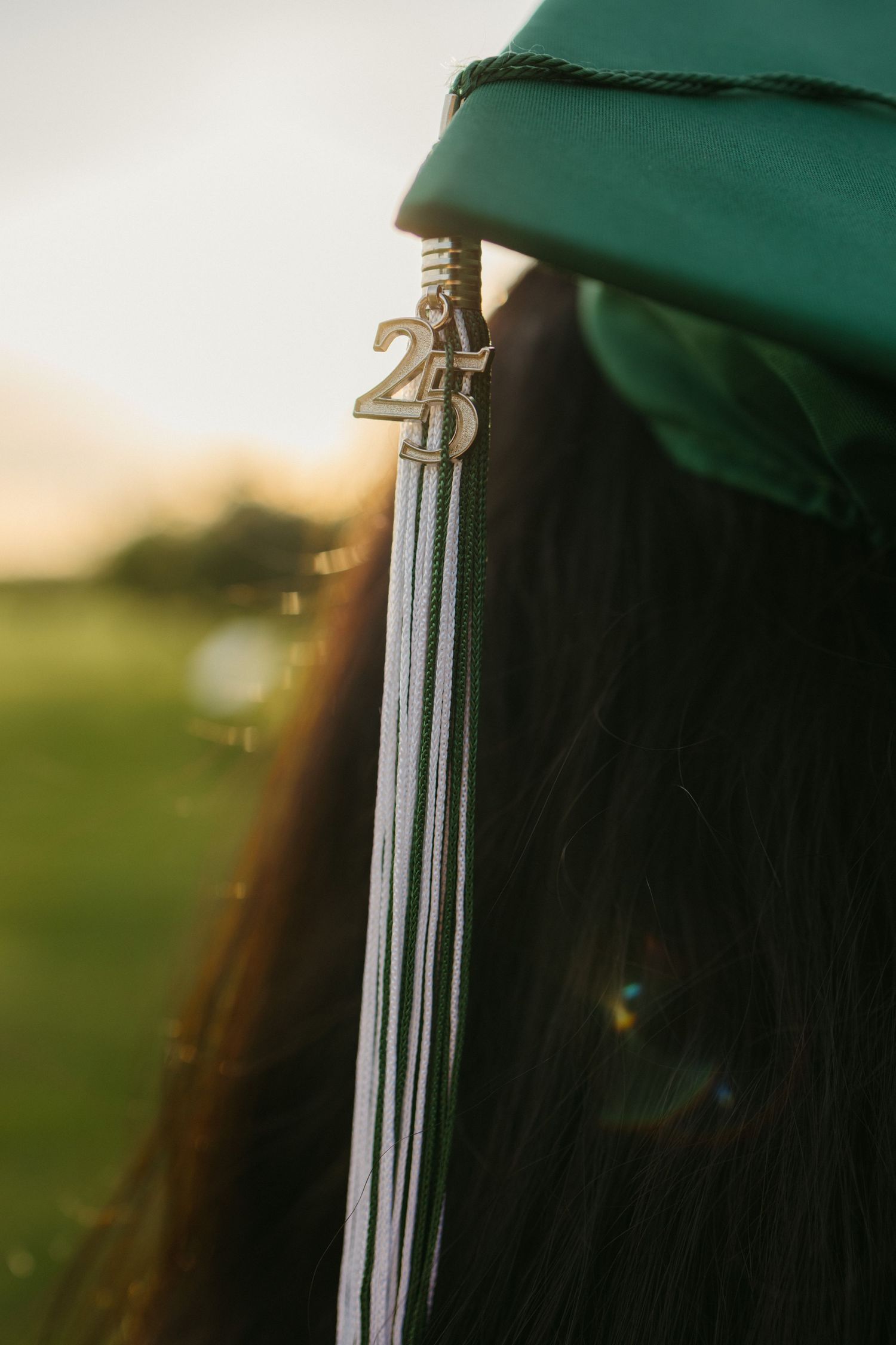 Close-up view of a graduation tassel with 2024 charm hanging from a green cap in golden sunlight.